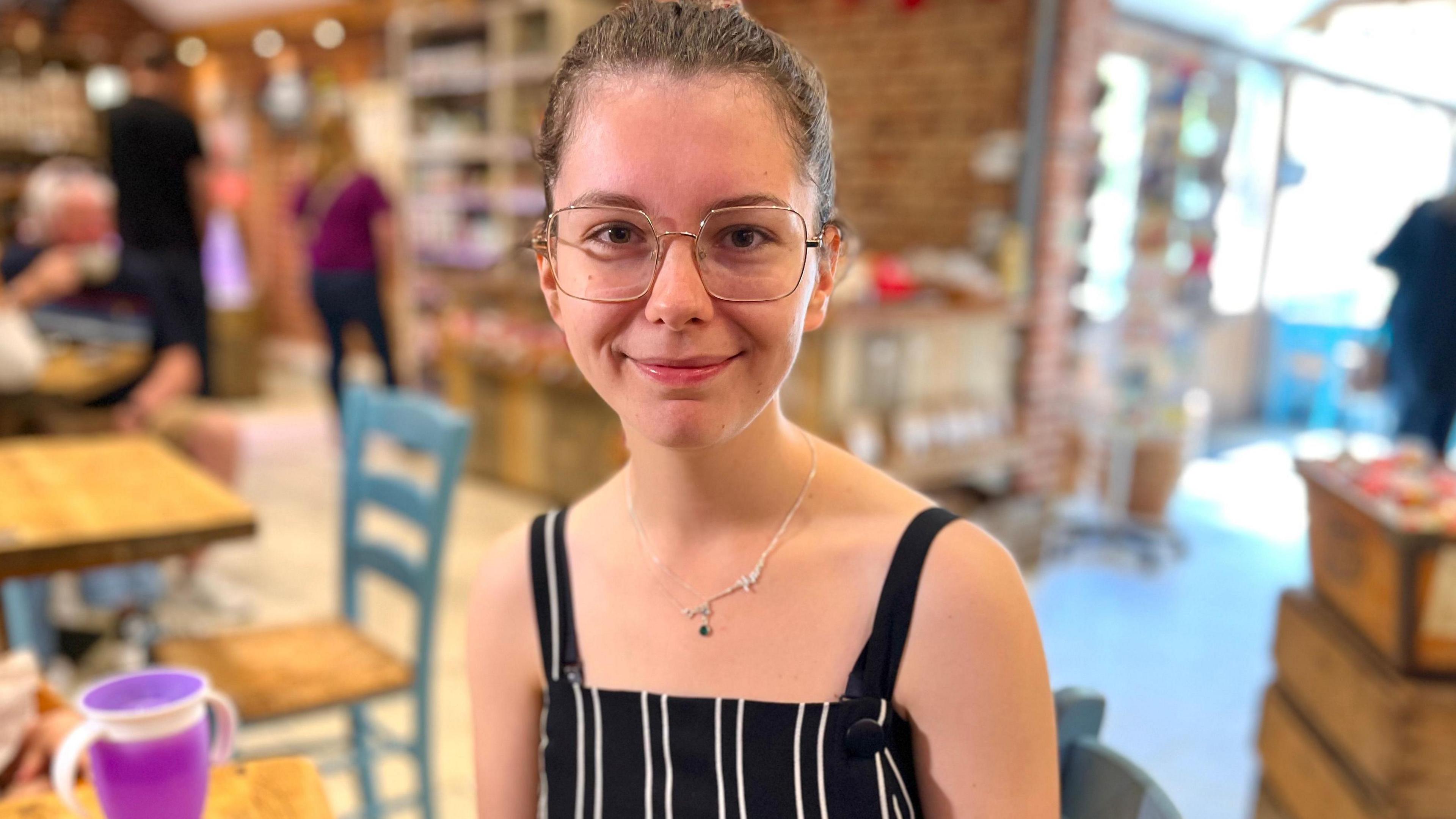 Georgia Hoyle has thin framed gold glasses and wears a black and white striped dungarees tunic