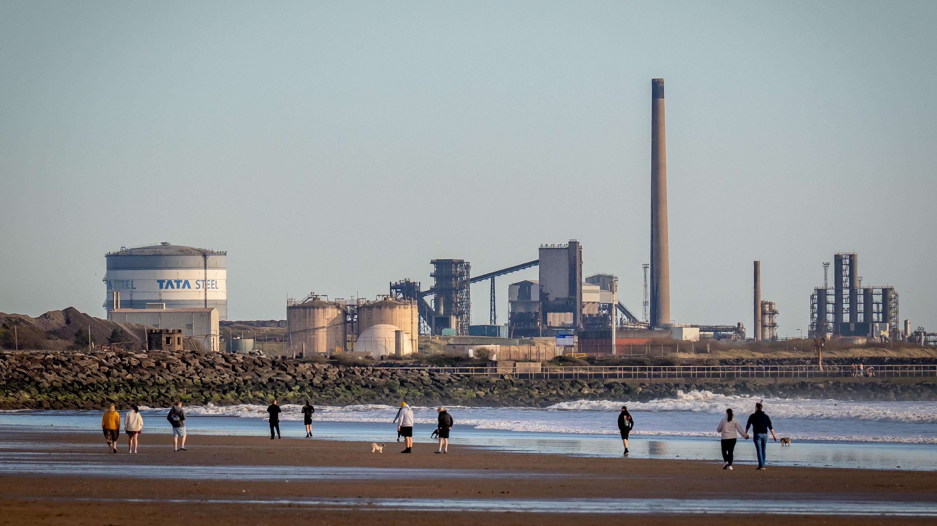 People walking along Abaravon Beach with the Tata Steelworks in the background.