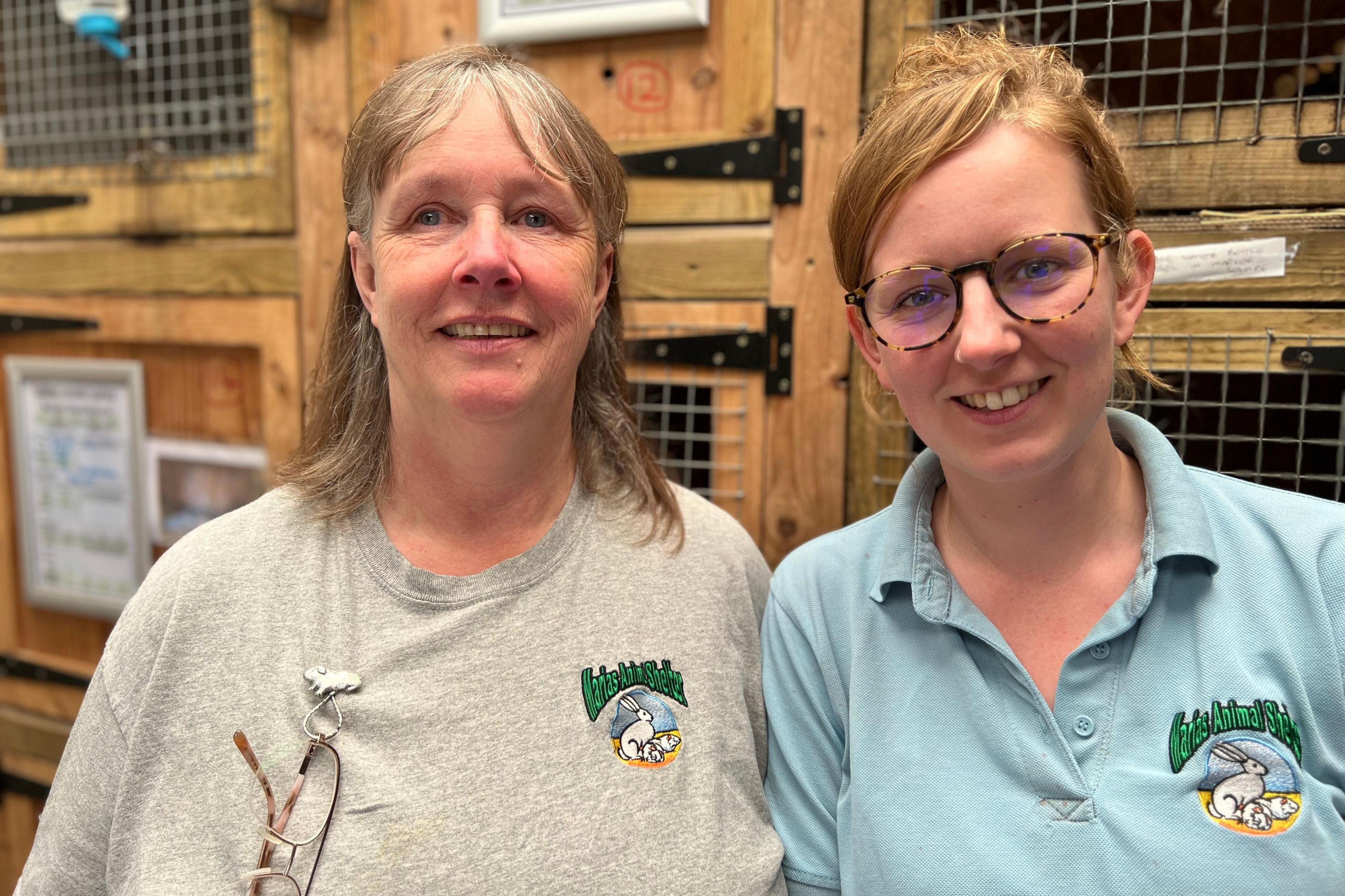 Two women pose for a photo beside hutches at Marias Animal Shelter
