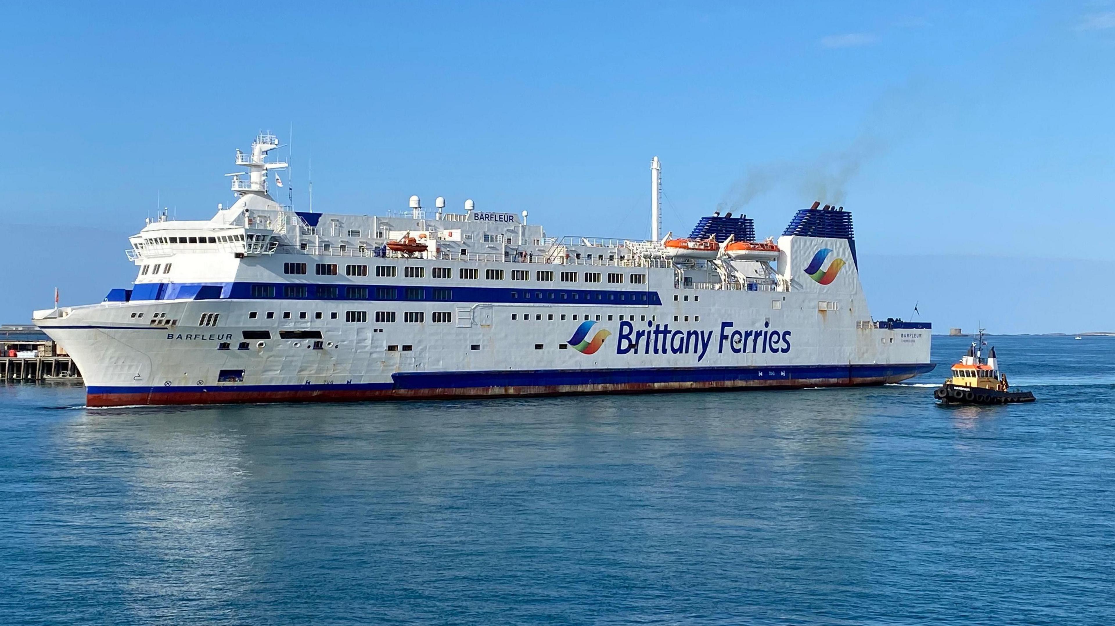 A white ferry with blue tipped chimneys with the words Brittany Ferries on the side arriving in St Peter Port Harbour.