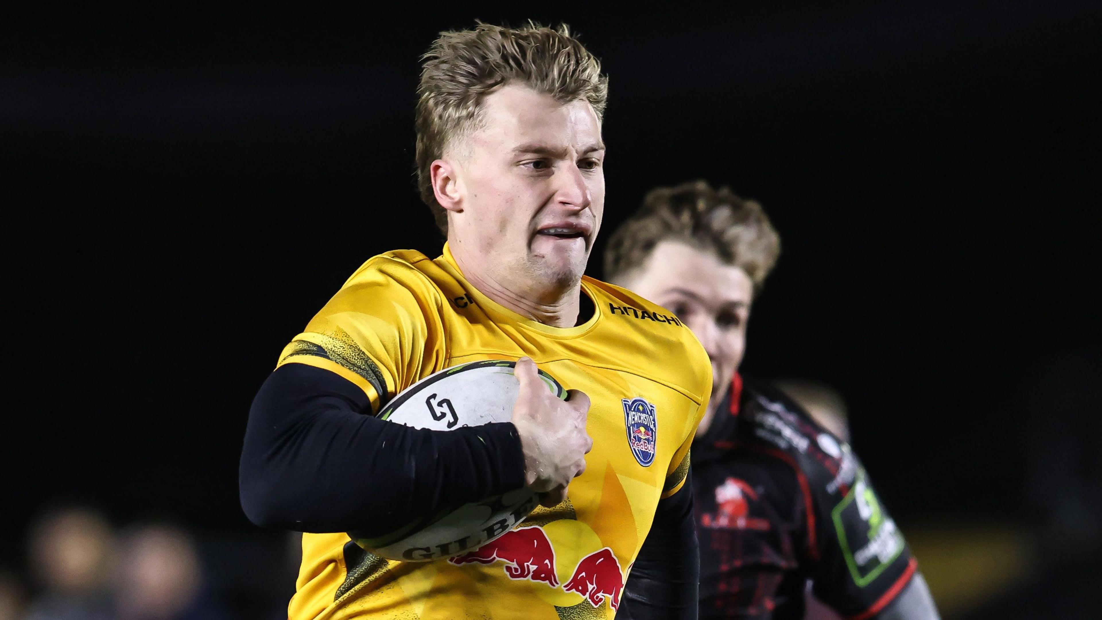 Alex Hearle, wearing Newcastle's yellow kit, running and carrying the rugby ball under his right arm