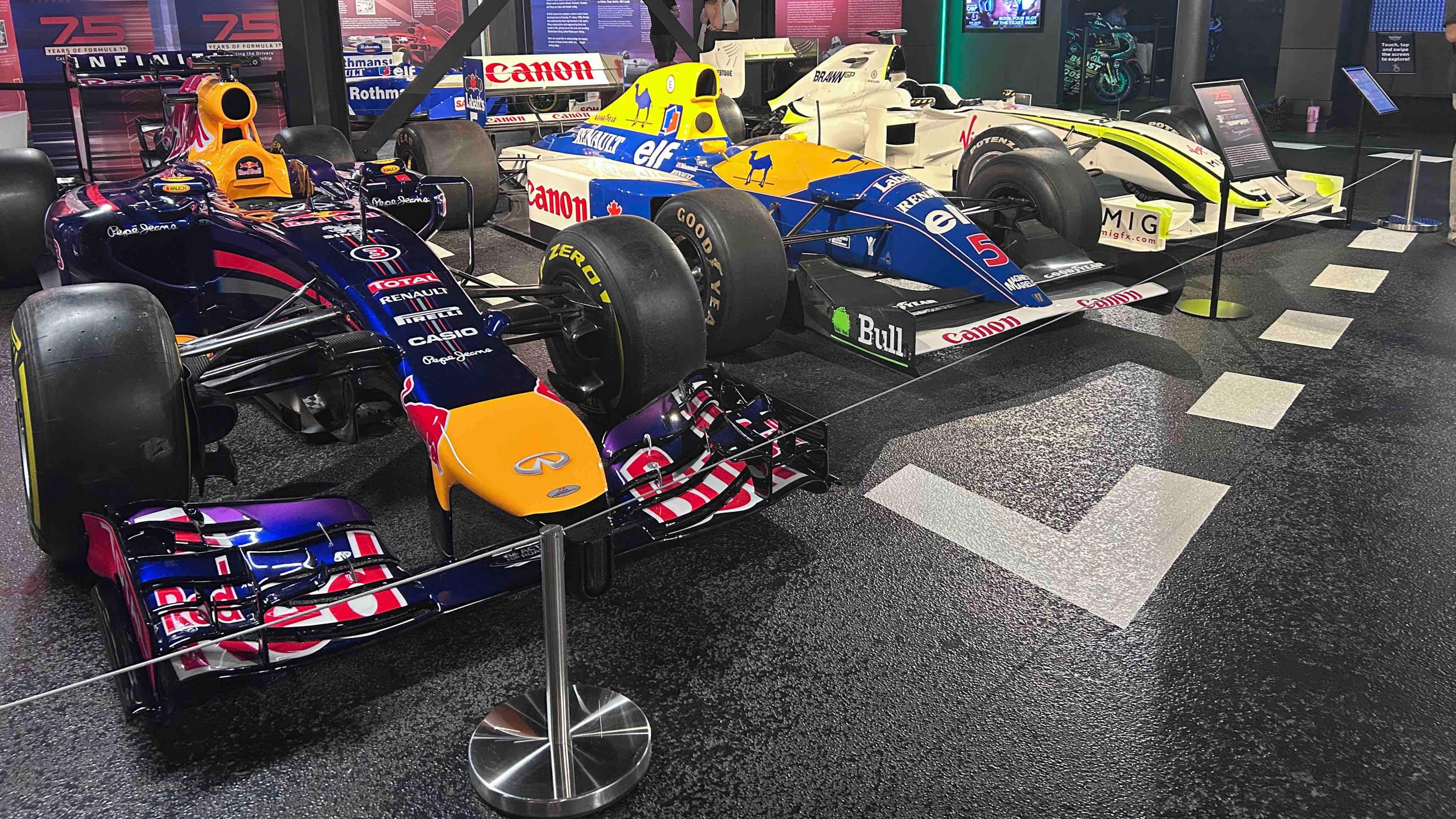 Nigel Mansell's car in the middle of two other F1 cars. It is blue and yellow and has Canon written across it.