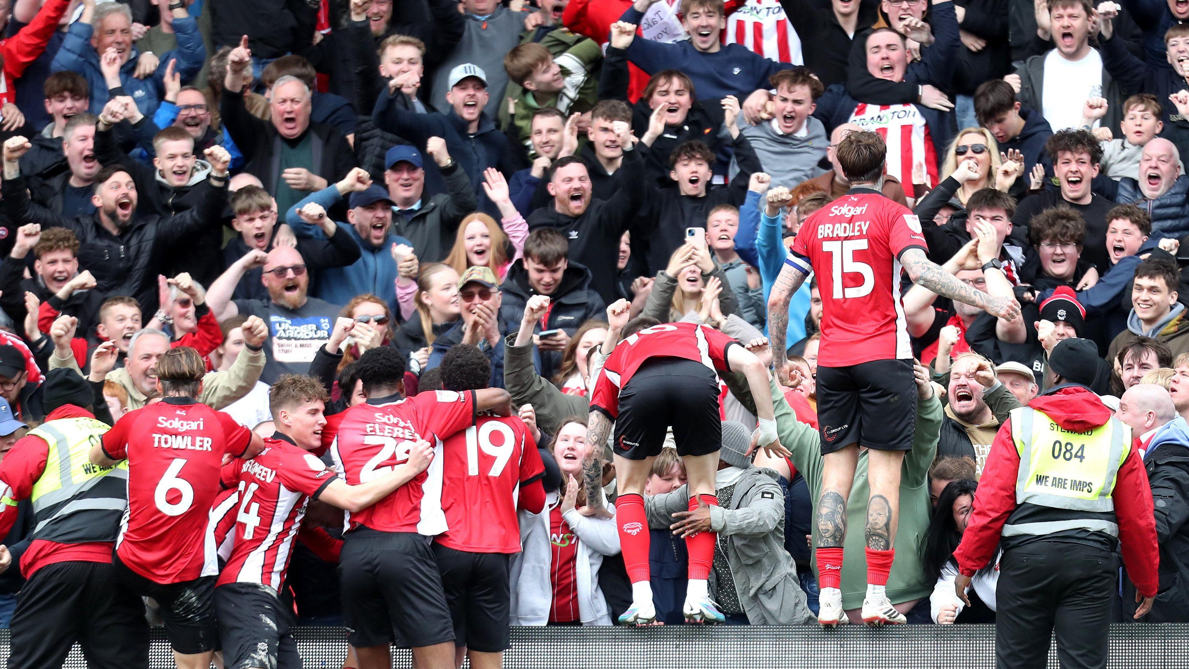 Lincoln City players, wearing their red and white home shirt, celebrate the winning goal over Wimbledon with their jubilant fans