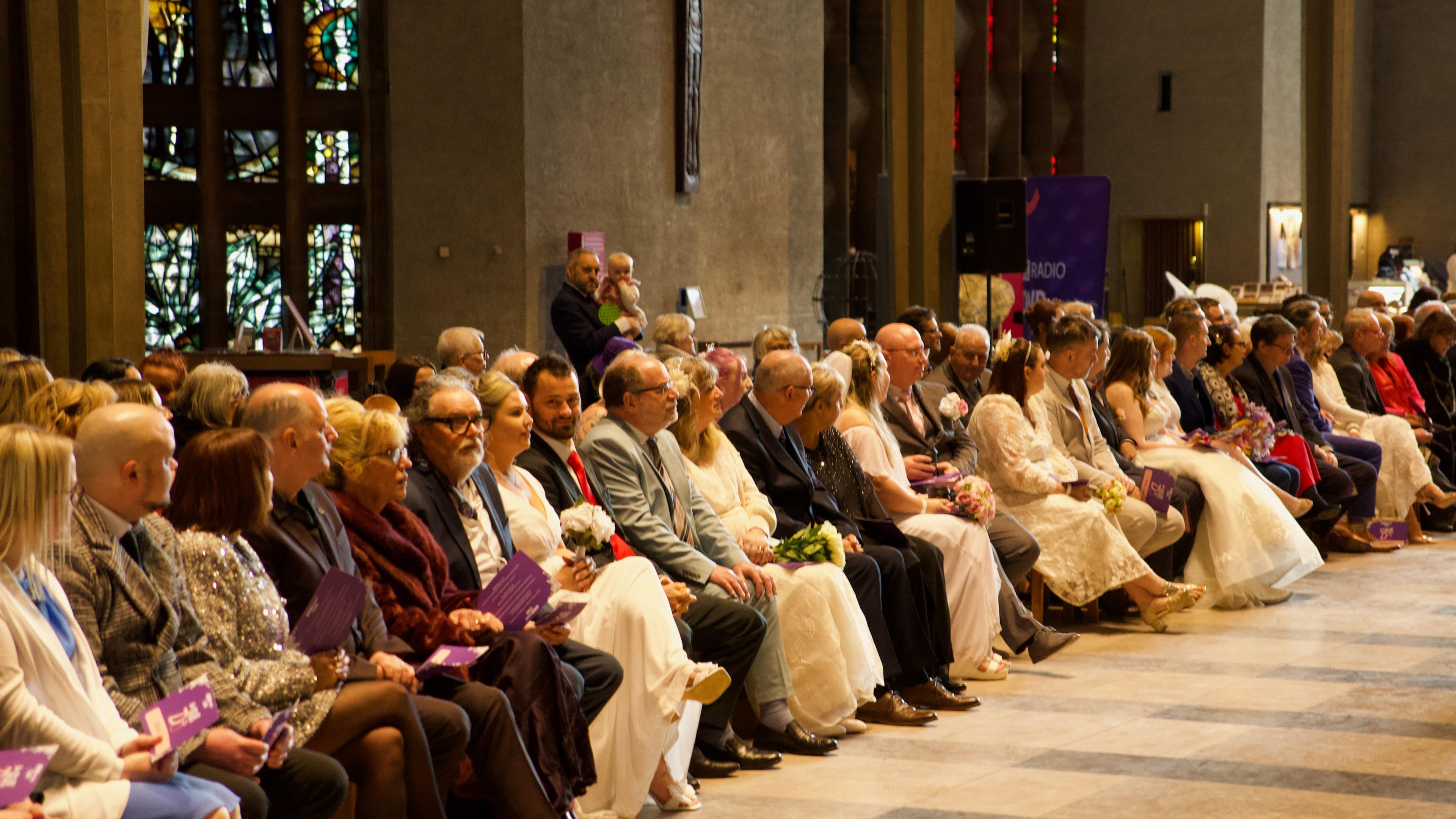 A line of guests at Coventry Cathedral wearing suits and wedding dresses