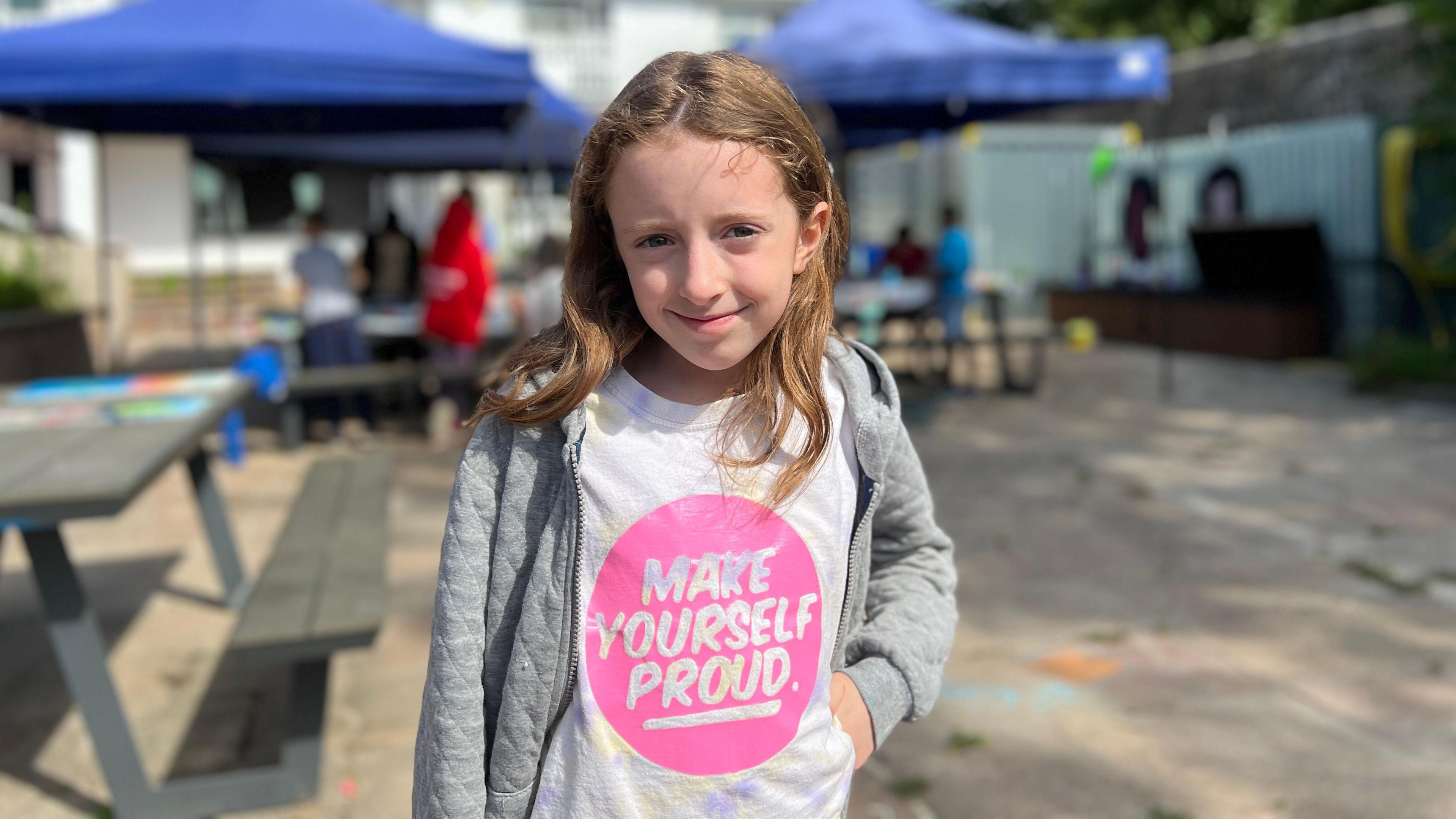 Emily smilies at the camera as she wears a 'Make Yourself Proud' top