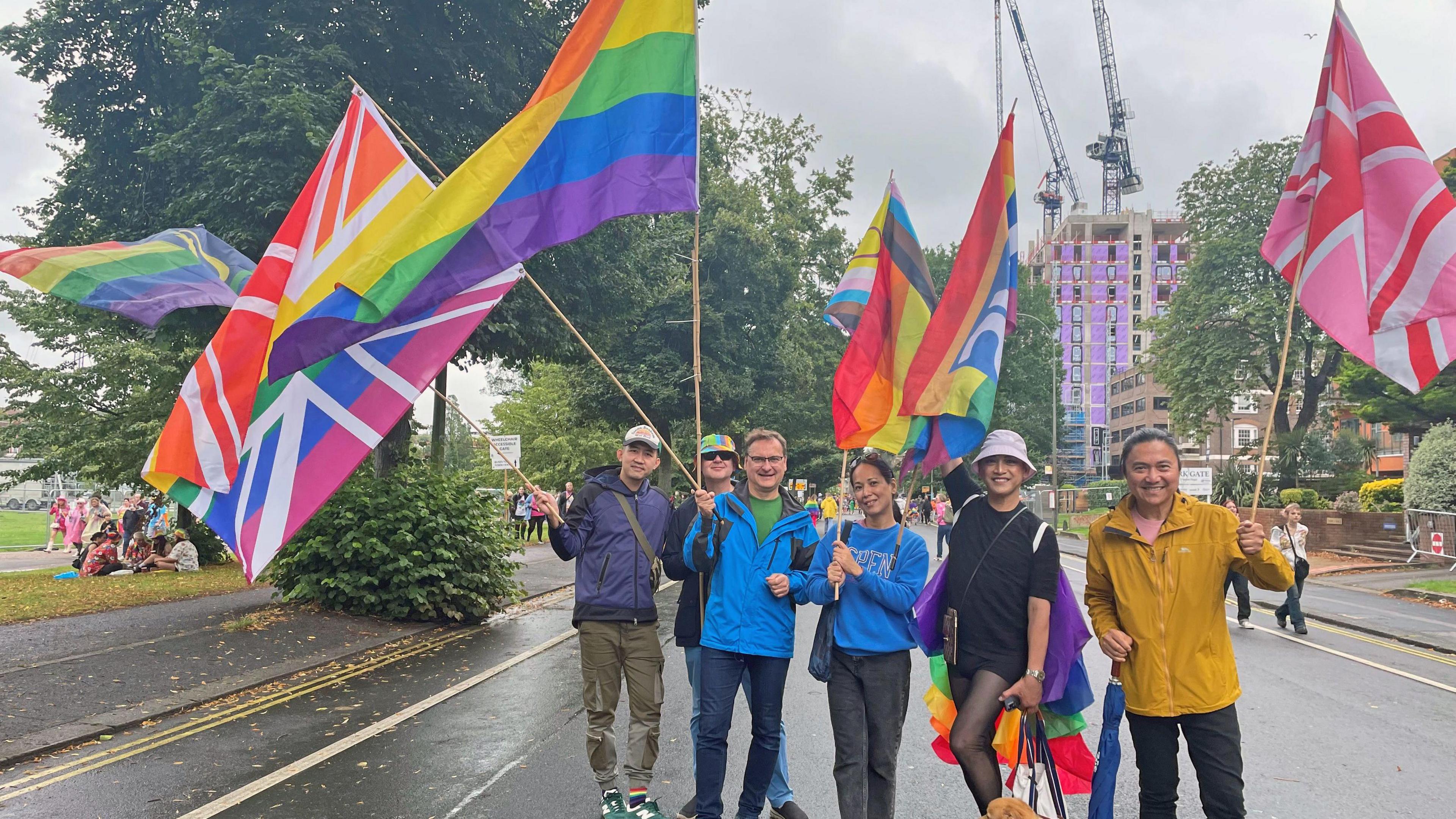 Six people holding large multicoloured flags walking in the street to celebrate Pride