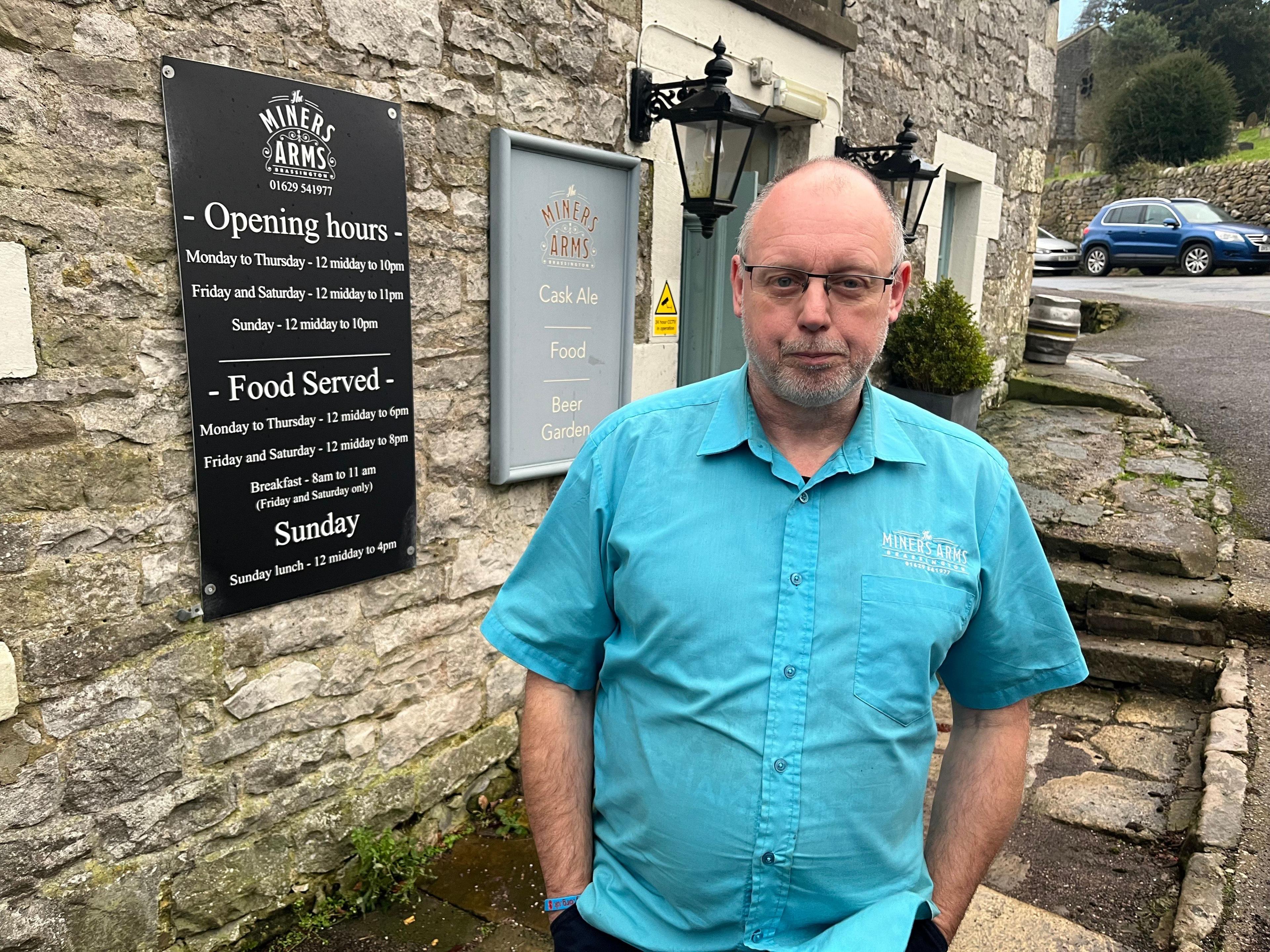 Trevor Howis is front of his pub. He is stood outside and is wearing a sky blue shirt.