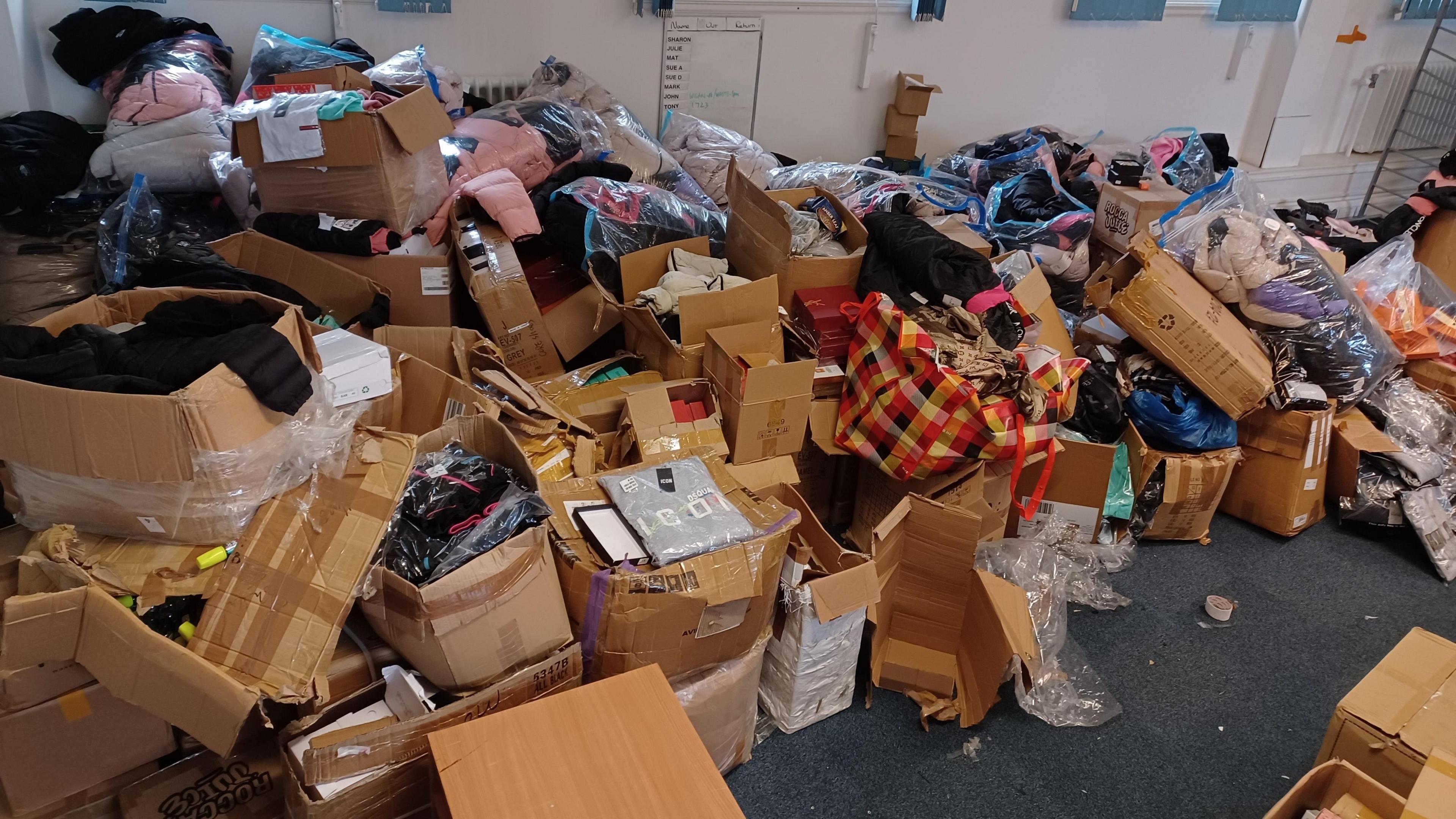 Cardboard boxes overflowing with fake designer goods stacked in the corner of a room