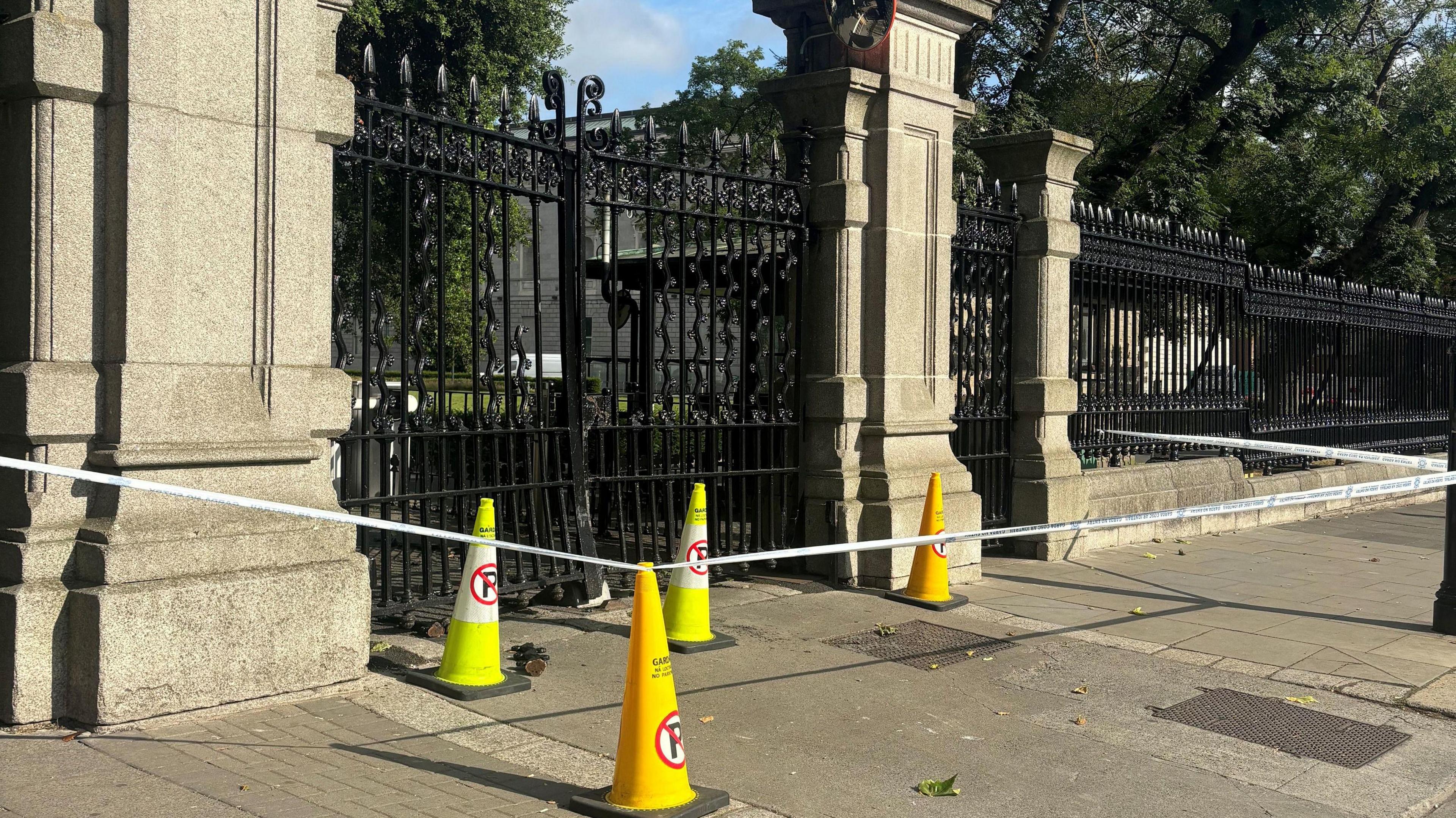 The scene after a vehicle drove into gates at Government Buildings in Dublin.  Police tape and cones are in front of a damaged gate.