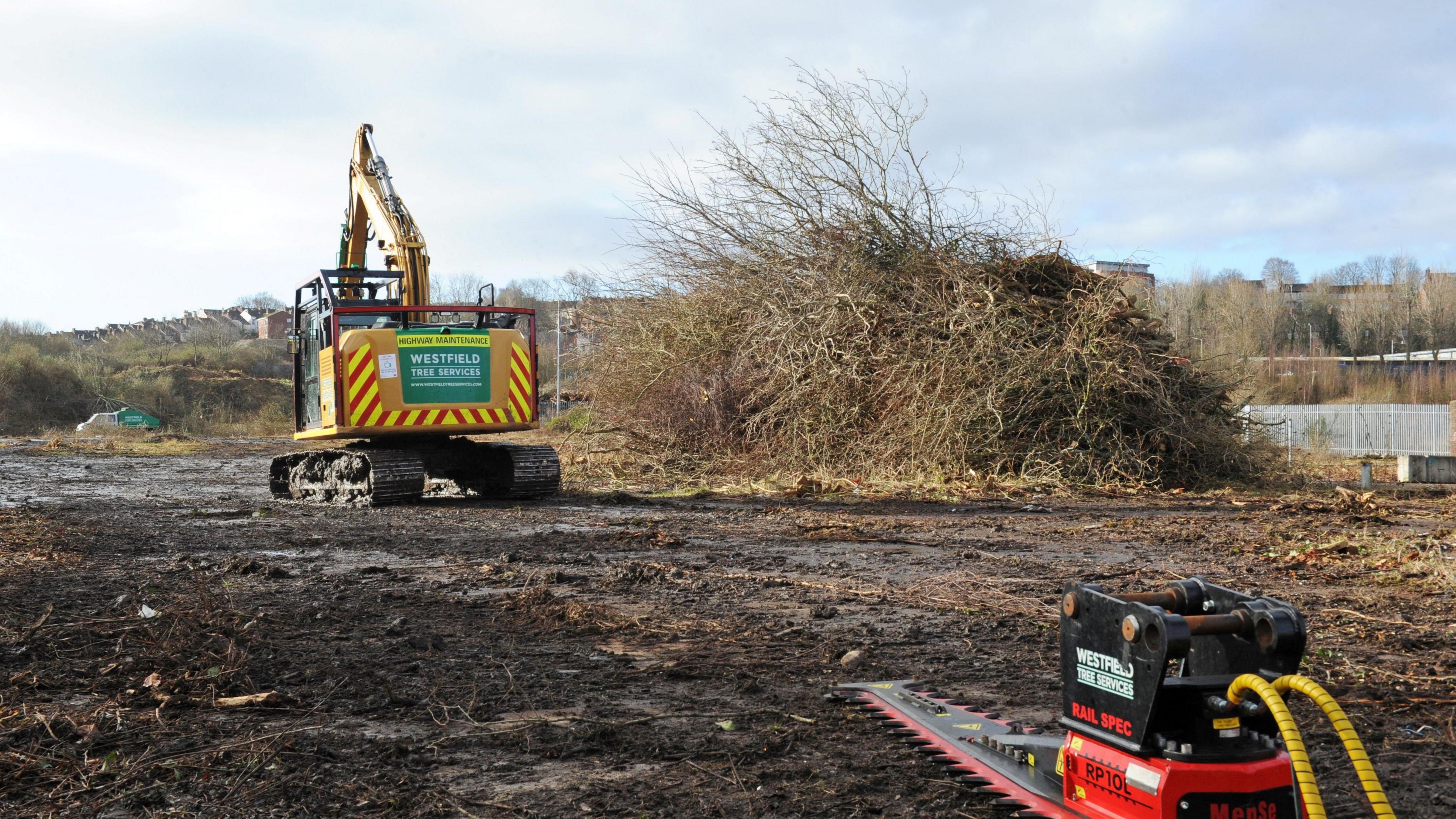 An empty plot of land being cleared for development with a digger in the middle distance and a power tool in the foreground
