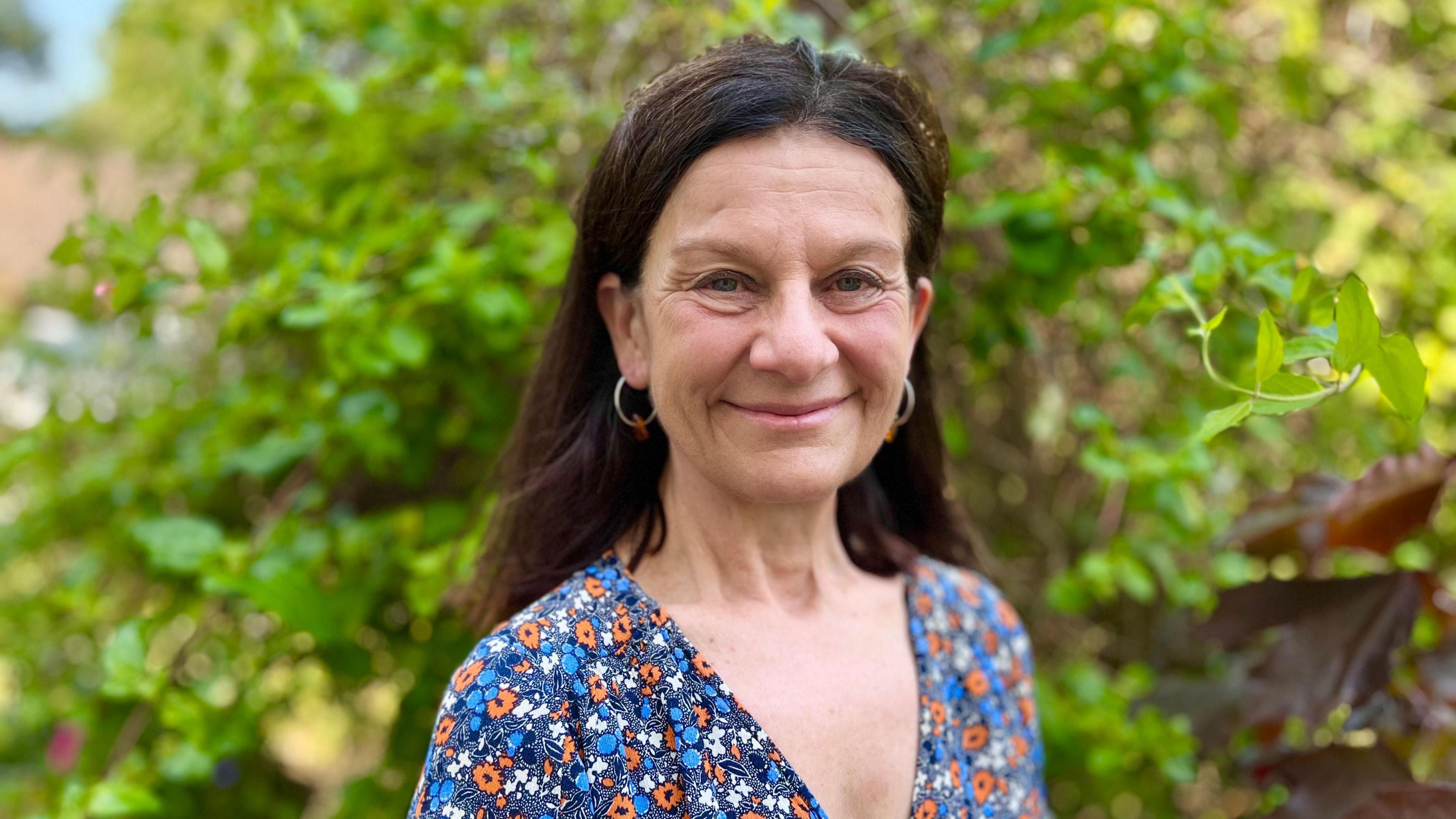 Profile picture of Bridget Smith she wears a v neck top with a flower pattern. Green foliage is in the background