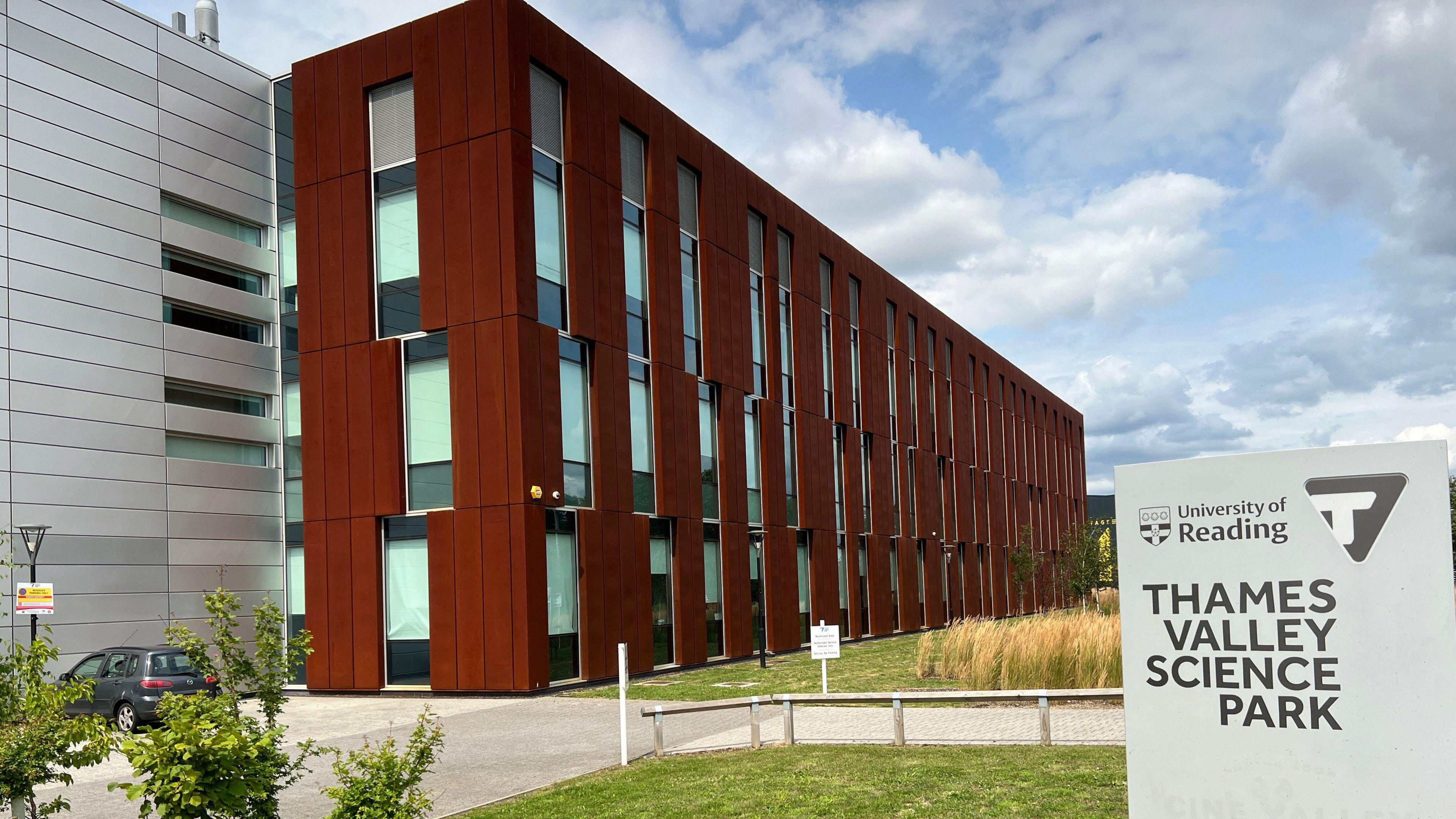 A sign saying Thames Valley Science Park. In the background are two modern looking buildings with green spaces in front of them.