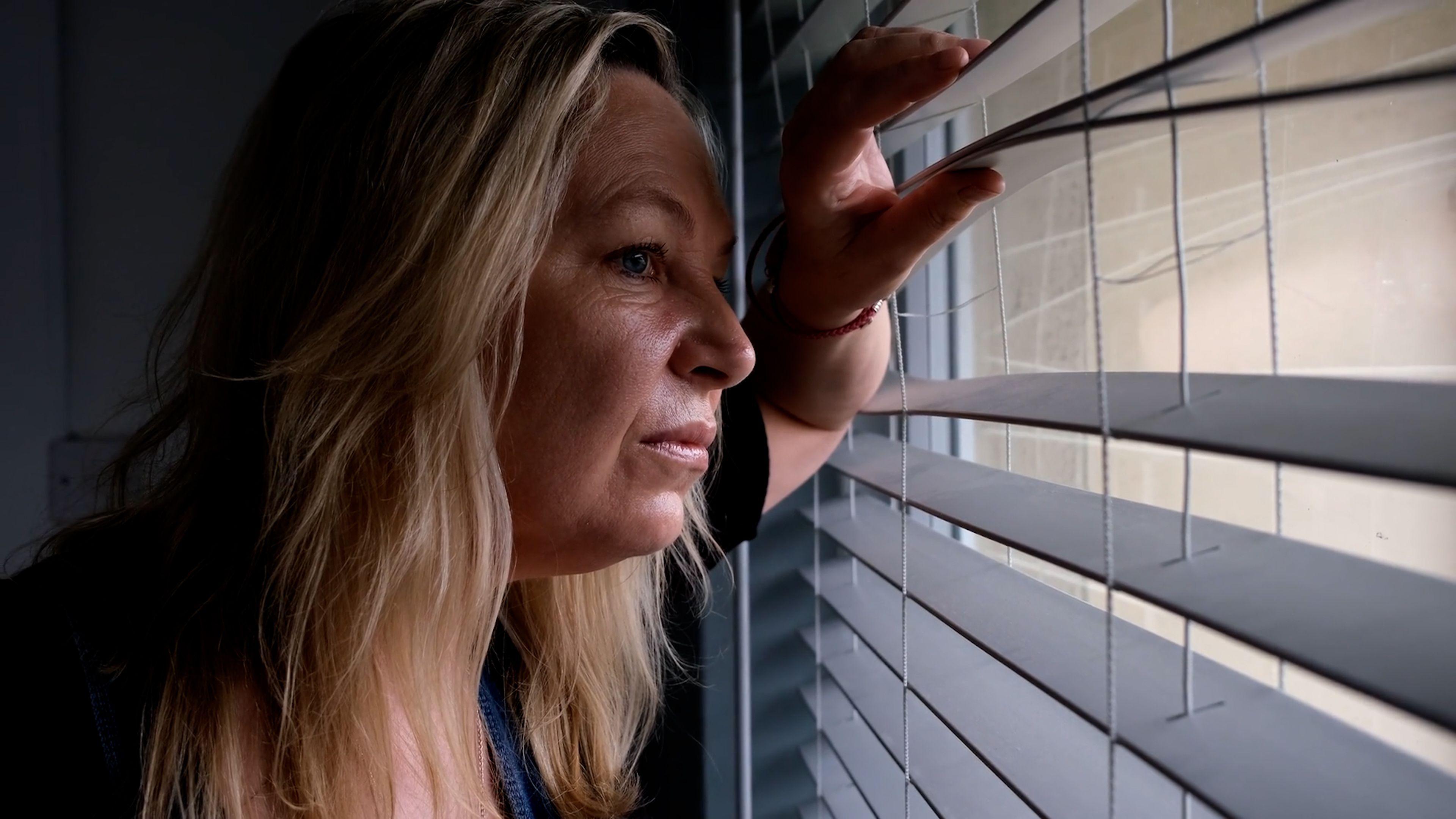 Catherine stares out of the window through her blinds