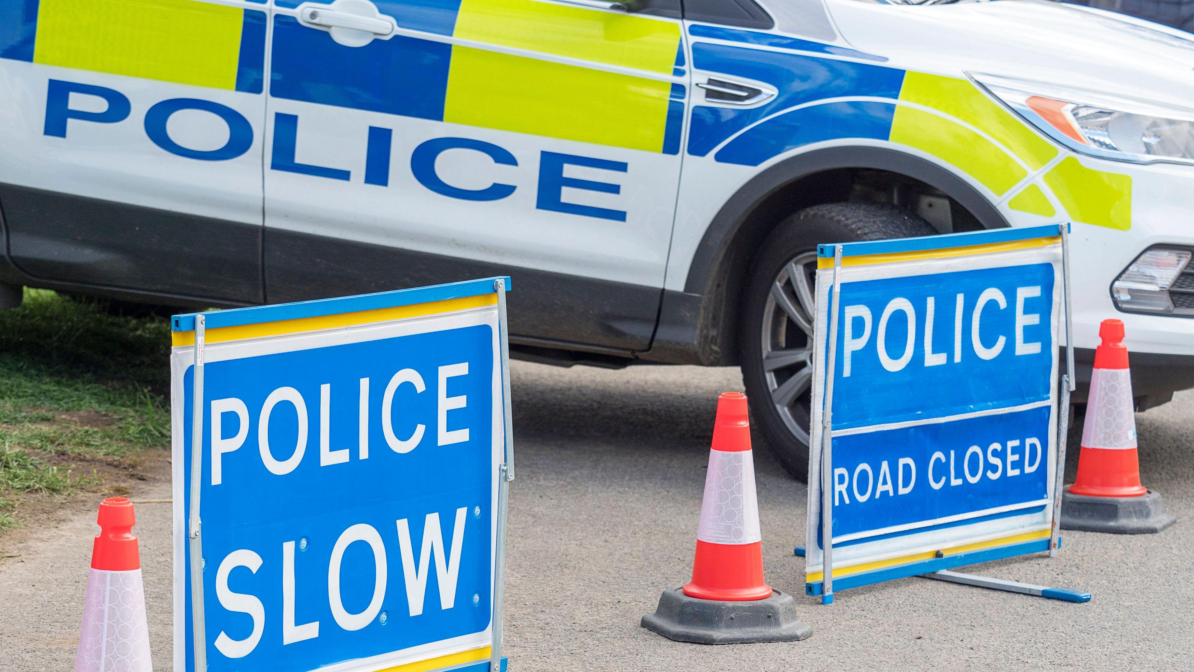 Close-up picture of police 'road closed' sign and 'police, slow' sign, in front of a police car