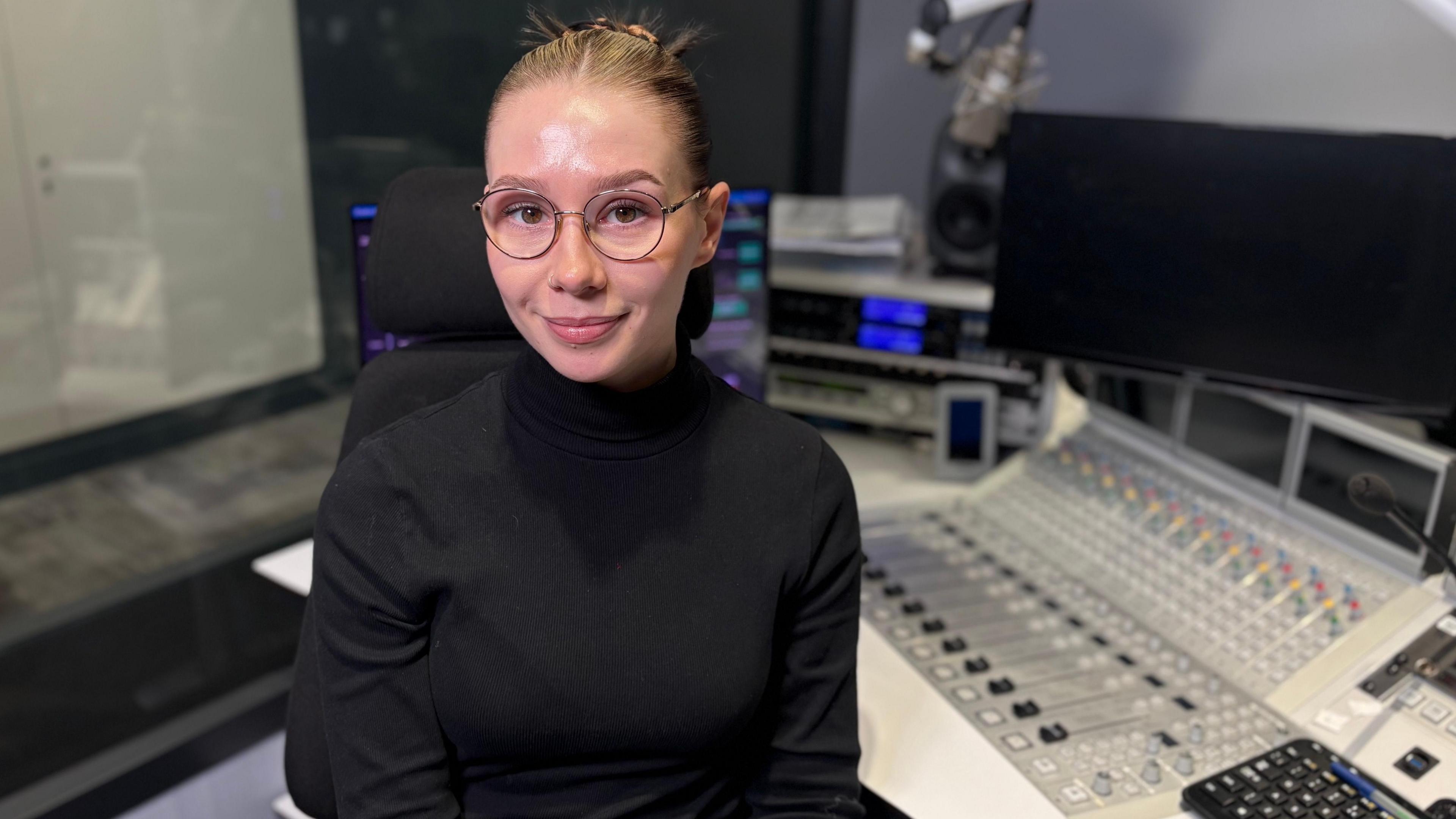 Llun o Molly yn eistedd ar gadair wrth ymyl desg stiwdio radio. Mae'n edrych at y camera. Mae ganddi wallt a llygaid brown a sbectol gron. Mae'n gwisgo siwmper du.