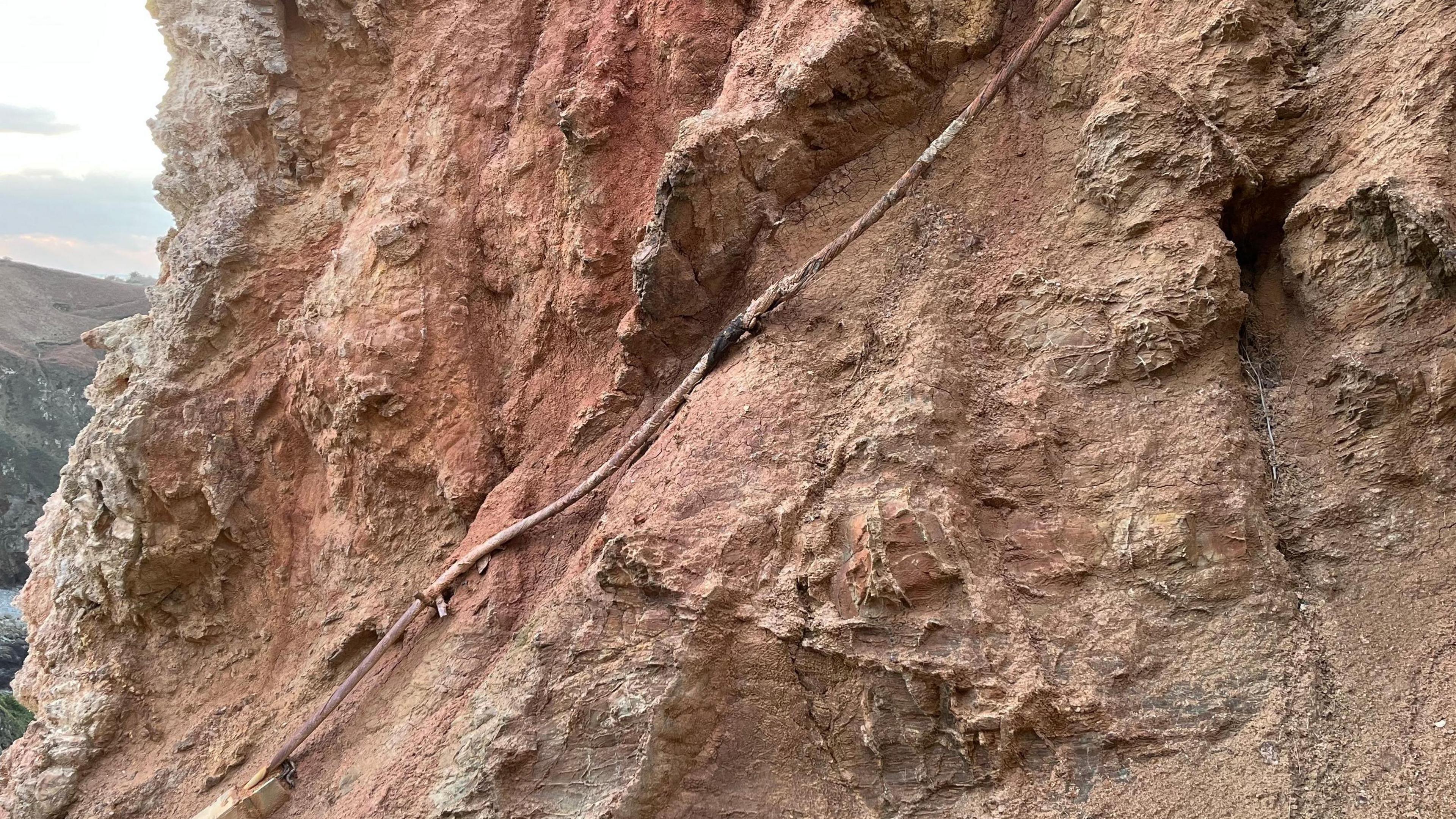 A fraying electricity cable tightly packed next to a clay covered wall.