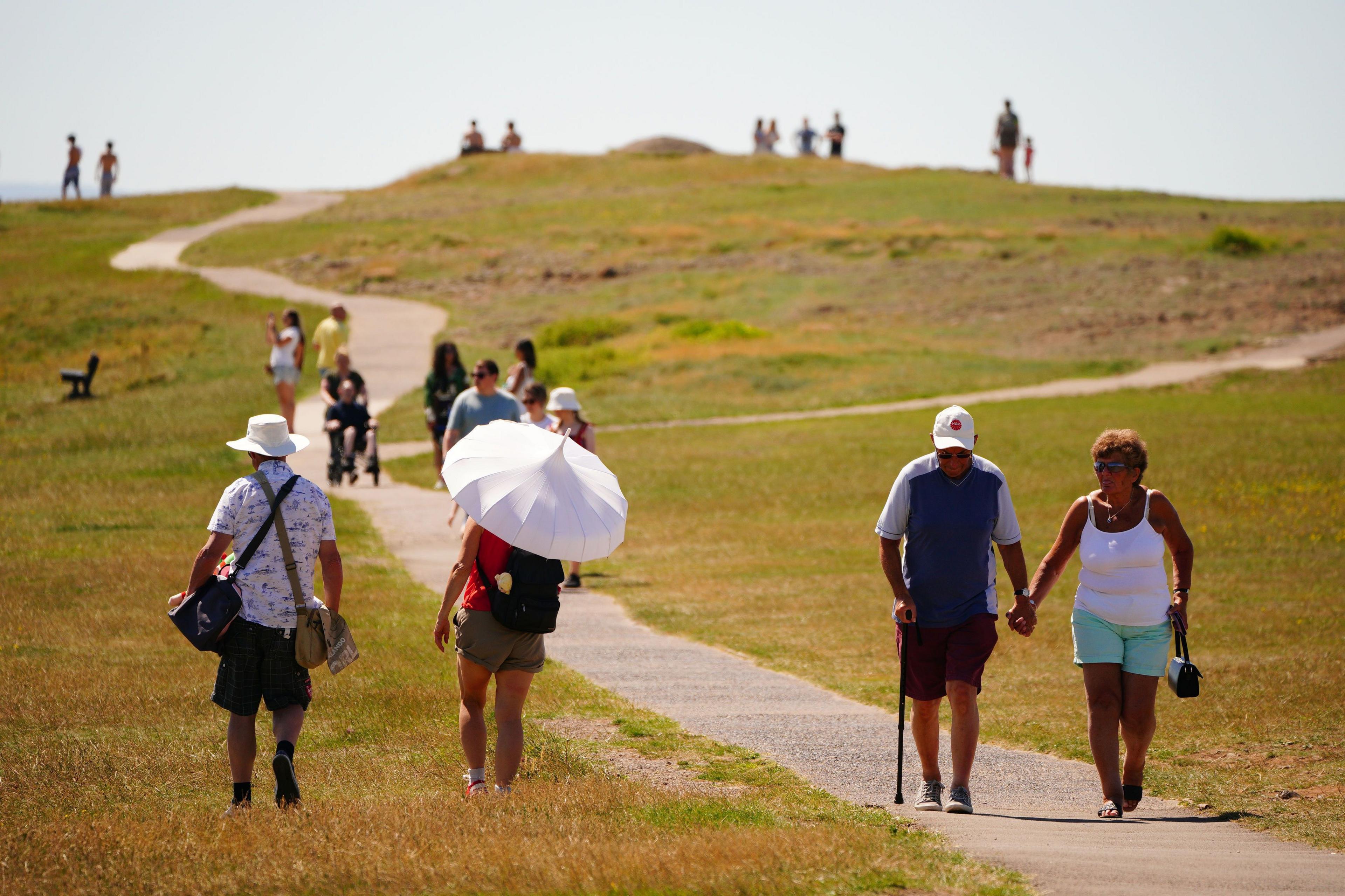 People are seen walking along a path. One woman is seen holding up an umbrella