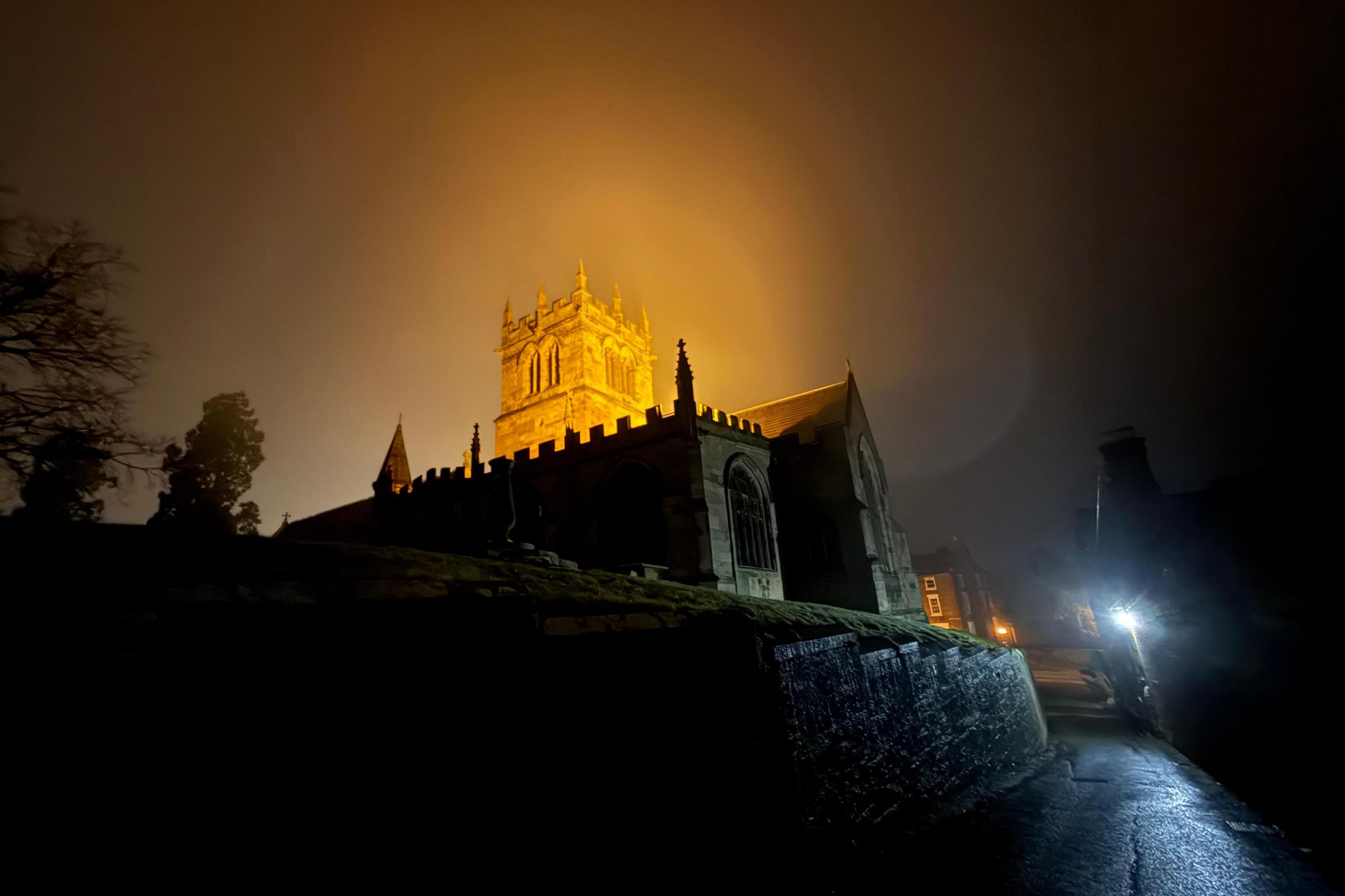 The tower of a church in Ellesmere is illuminated with a glow on a dark night 