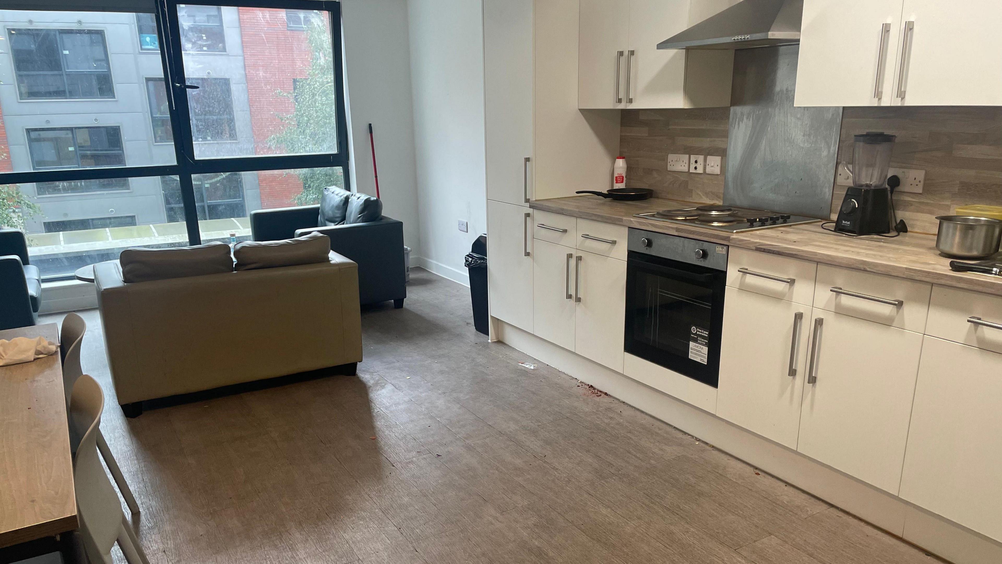 A basic kitchen with two sofas at the far side in front of a large windown