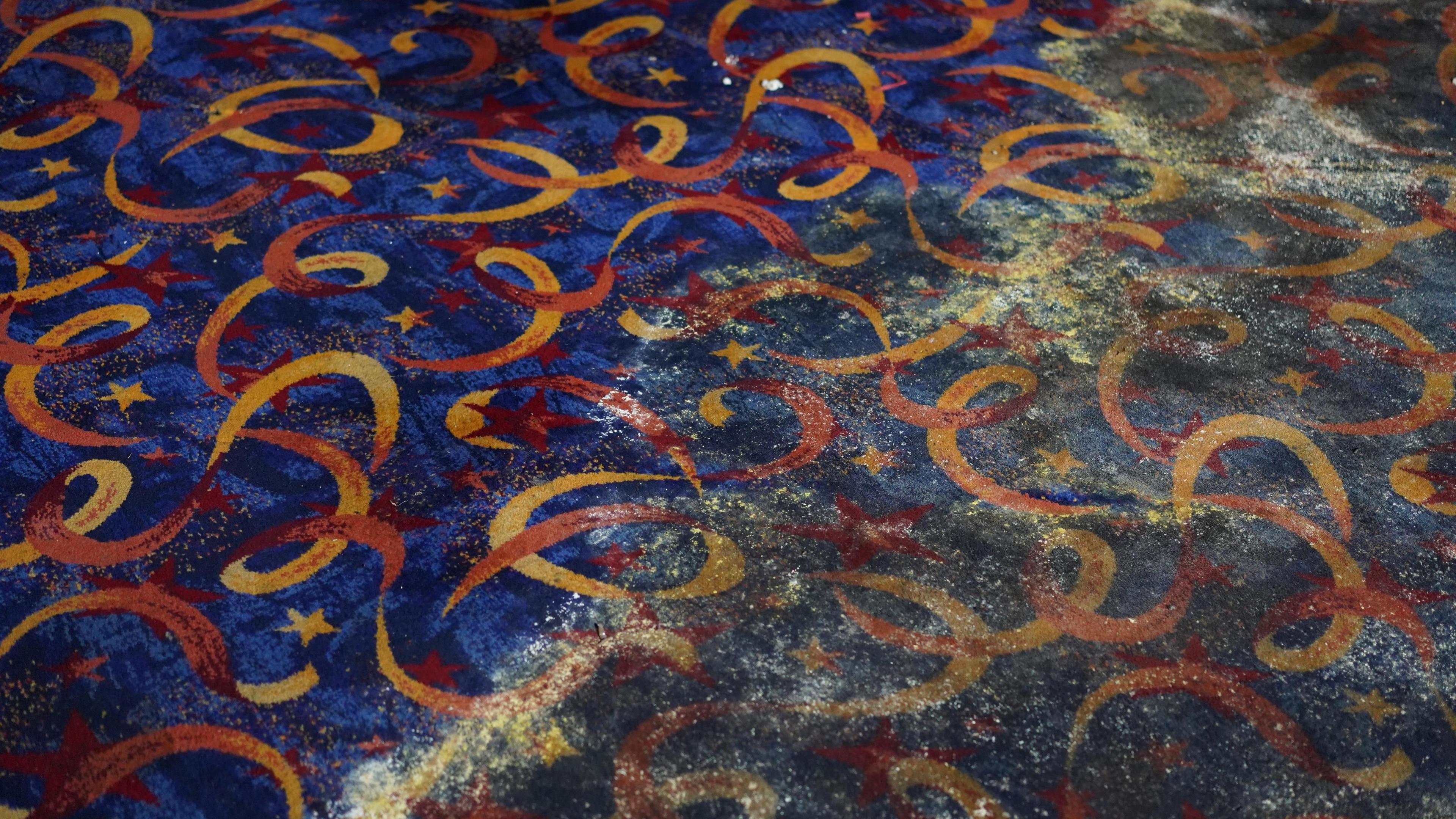 A blue, yellow and orange patterned carpet is covered in dirt and mould.