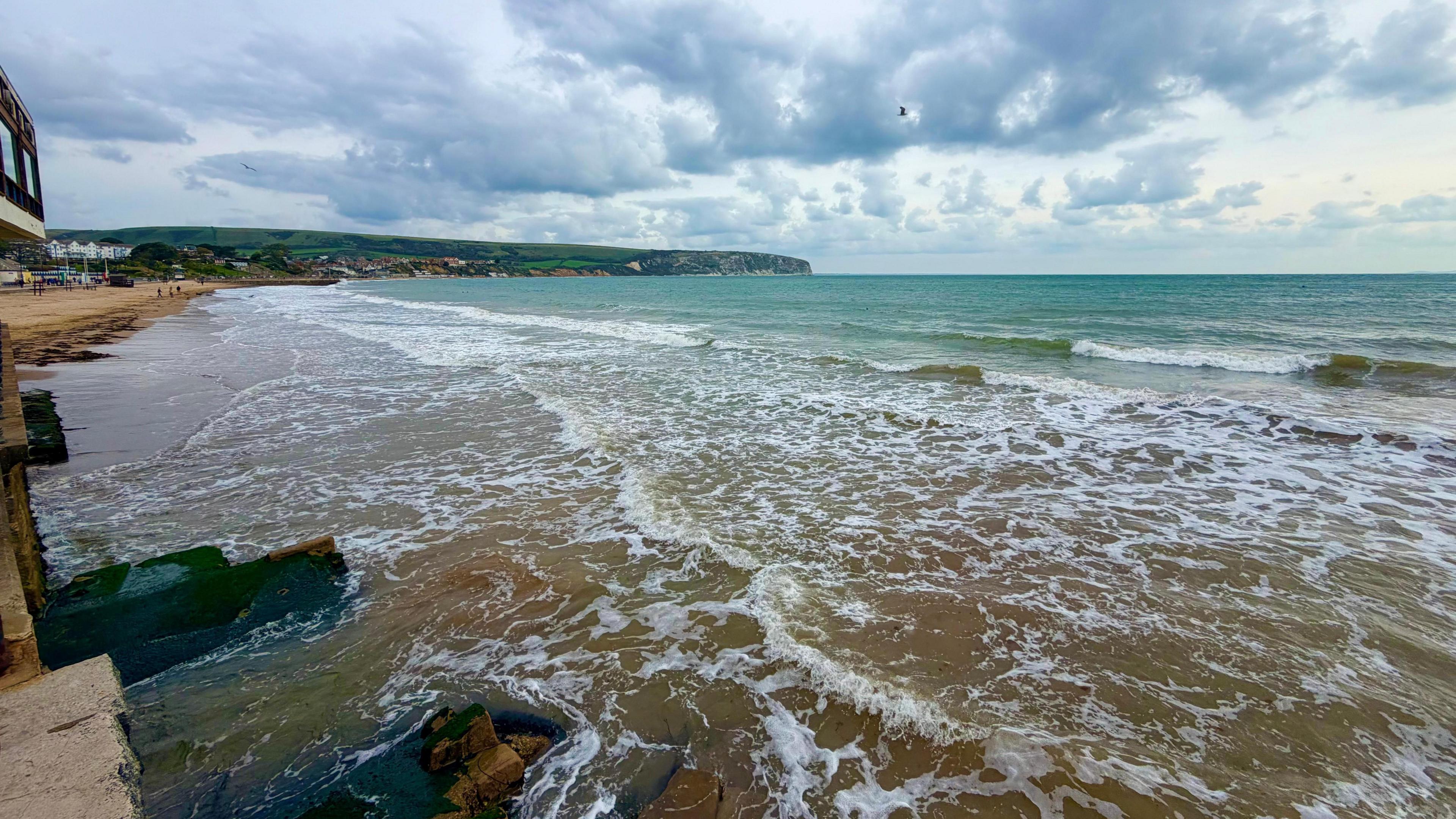 Gentle, small waves lapping onto the beach at Swanage with low cloud above the sea.