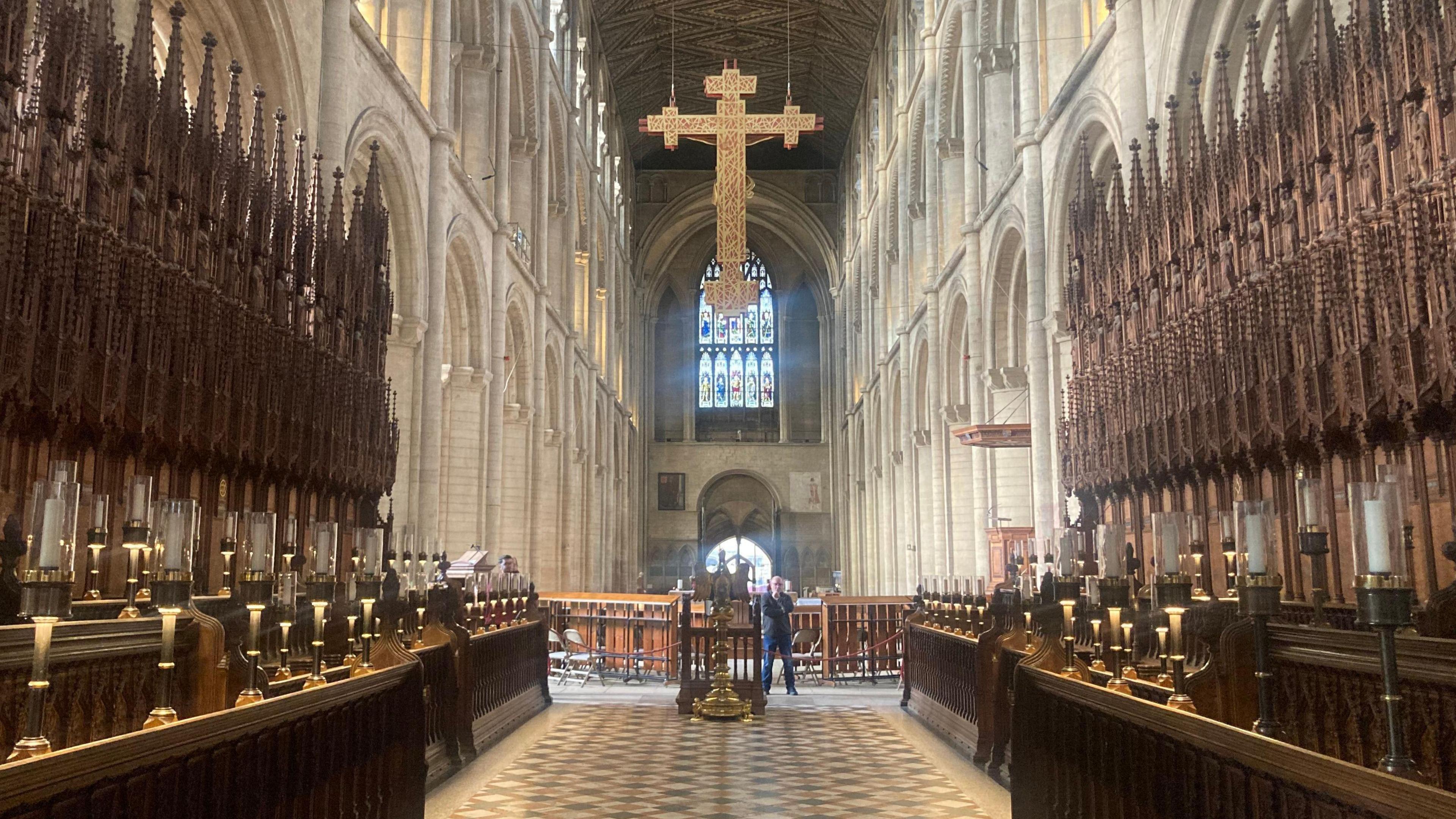 The nave of Peterborough Cathedral, with a big golden cross hanging from the ceiling.