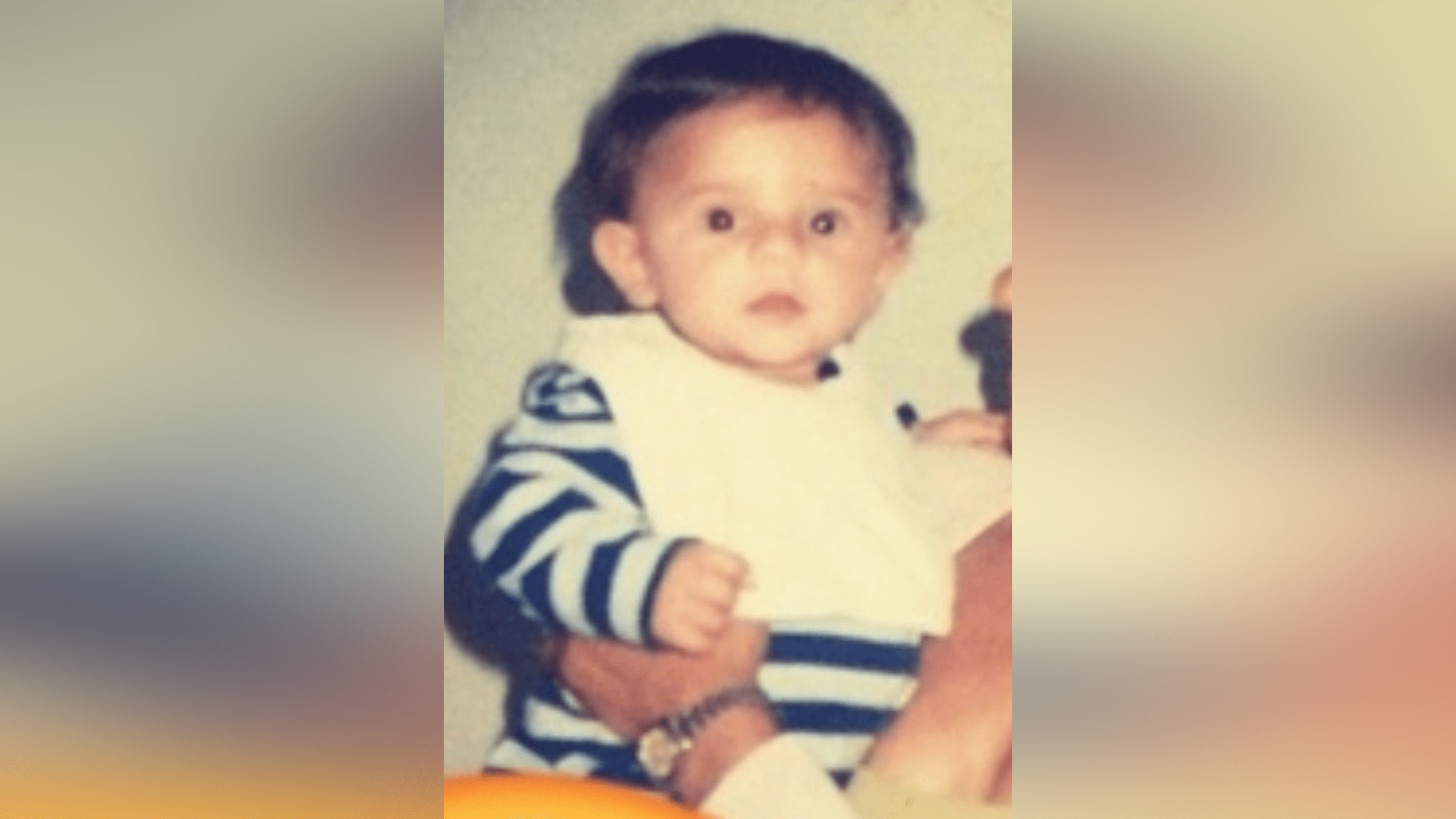 Oliver Archer as a young child. He wears a striped top and a white bib.