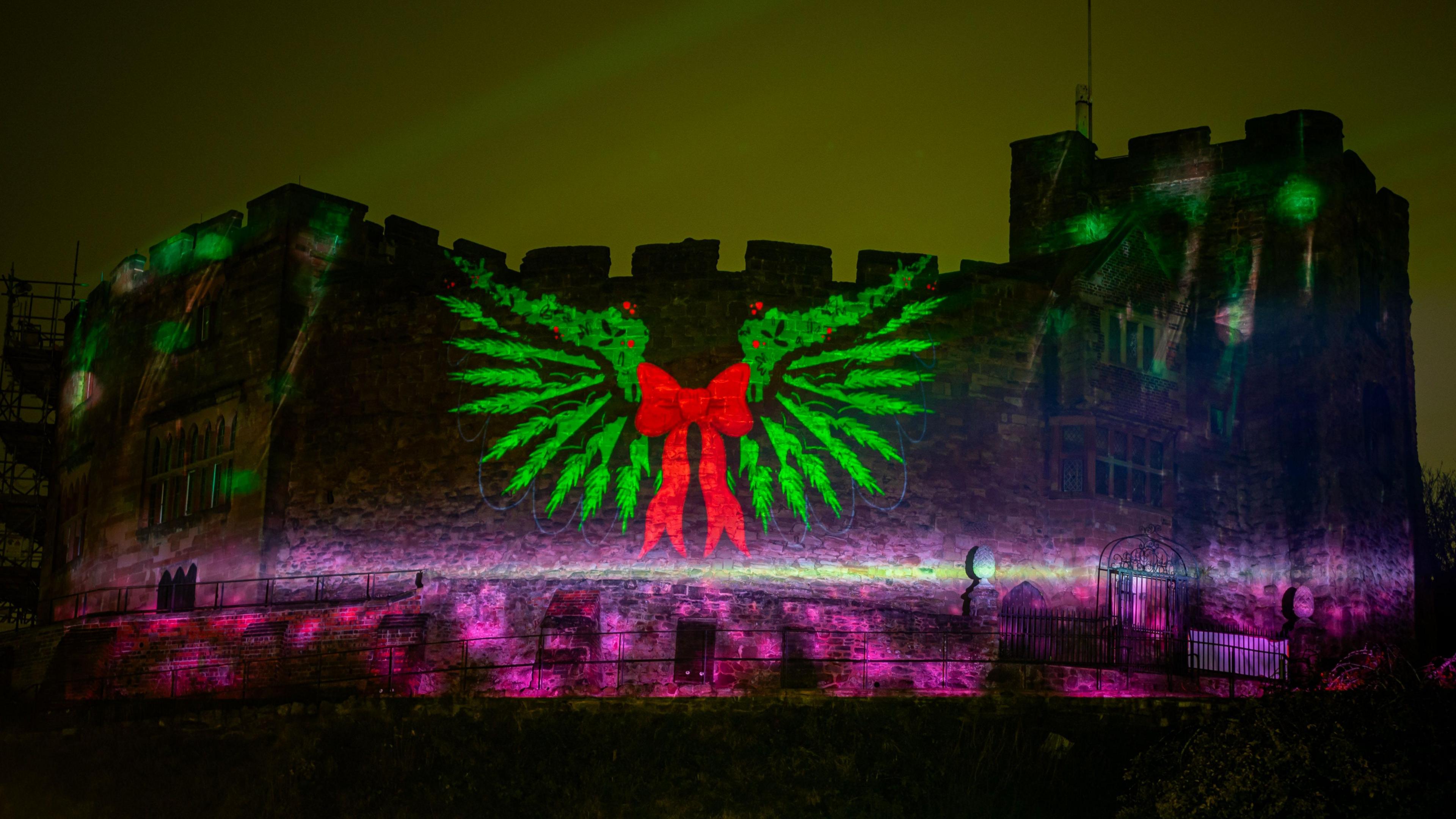 Tamworth Castle, viewed at night from below, is illuminated with an image of a green wreath with a red bow on the walls.