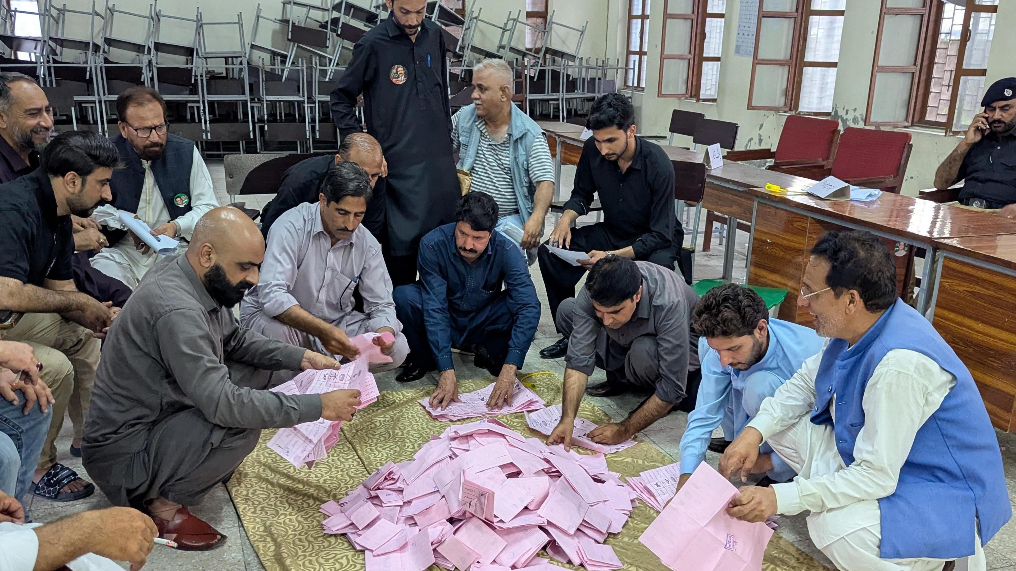 Election officials crouch round a pile of pink ballot papers as they count votes in the local elections in Muzaffarabad, the capital of Pakistan-administered Kashmir.
