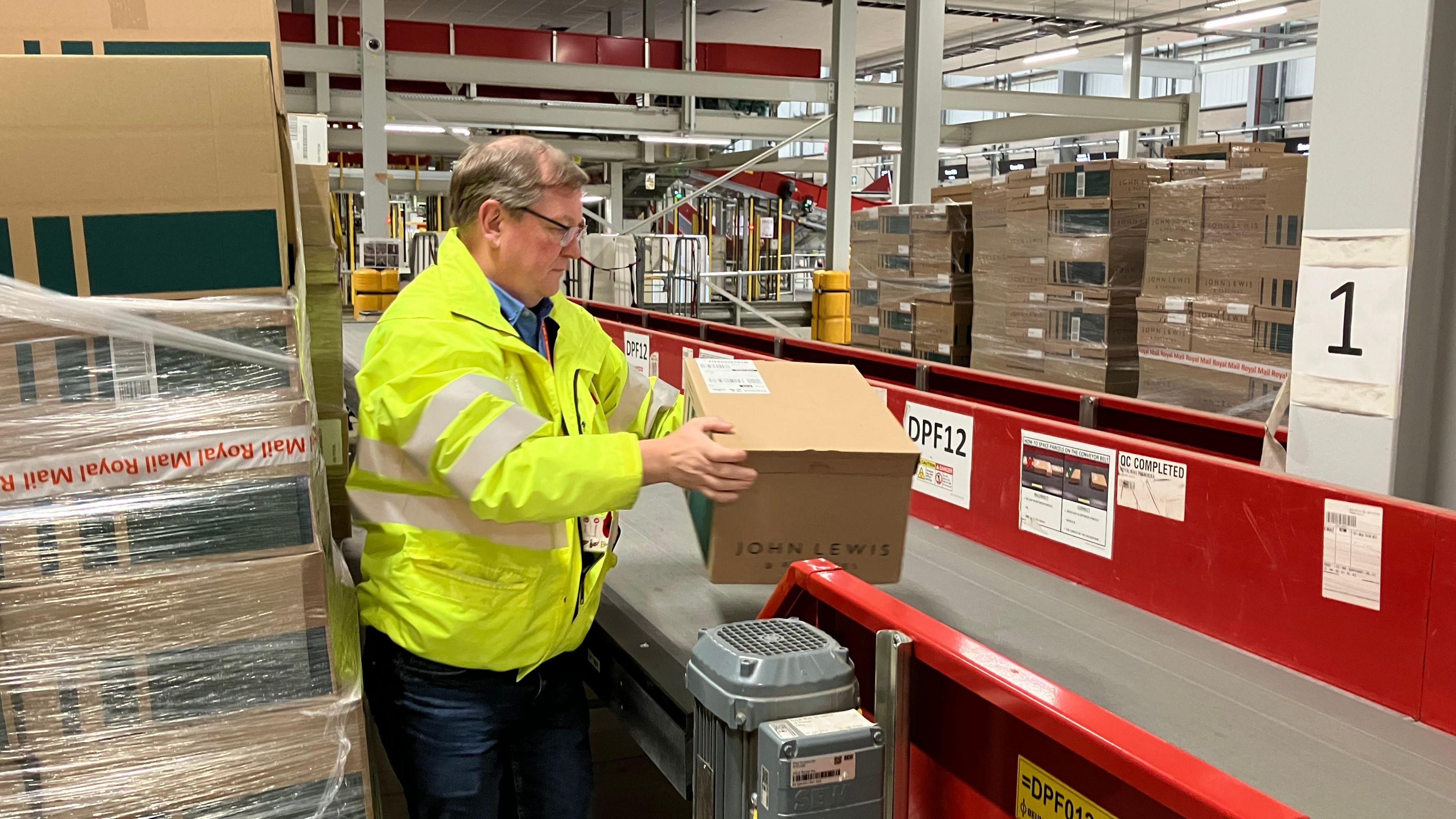 A man handles a medium size parcel as it moves along a conveyor belt.