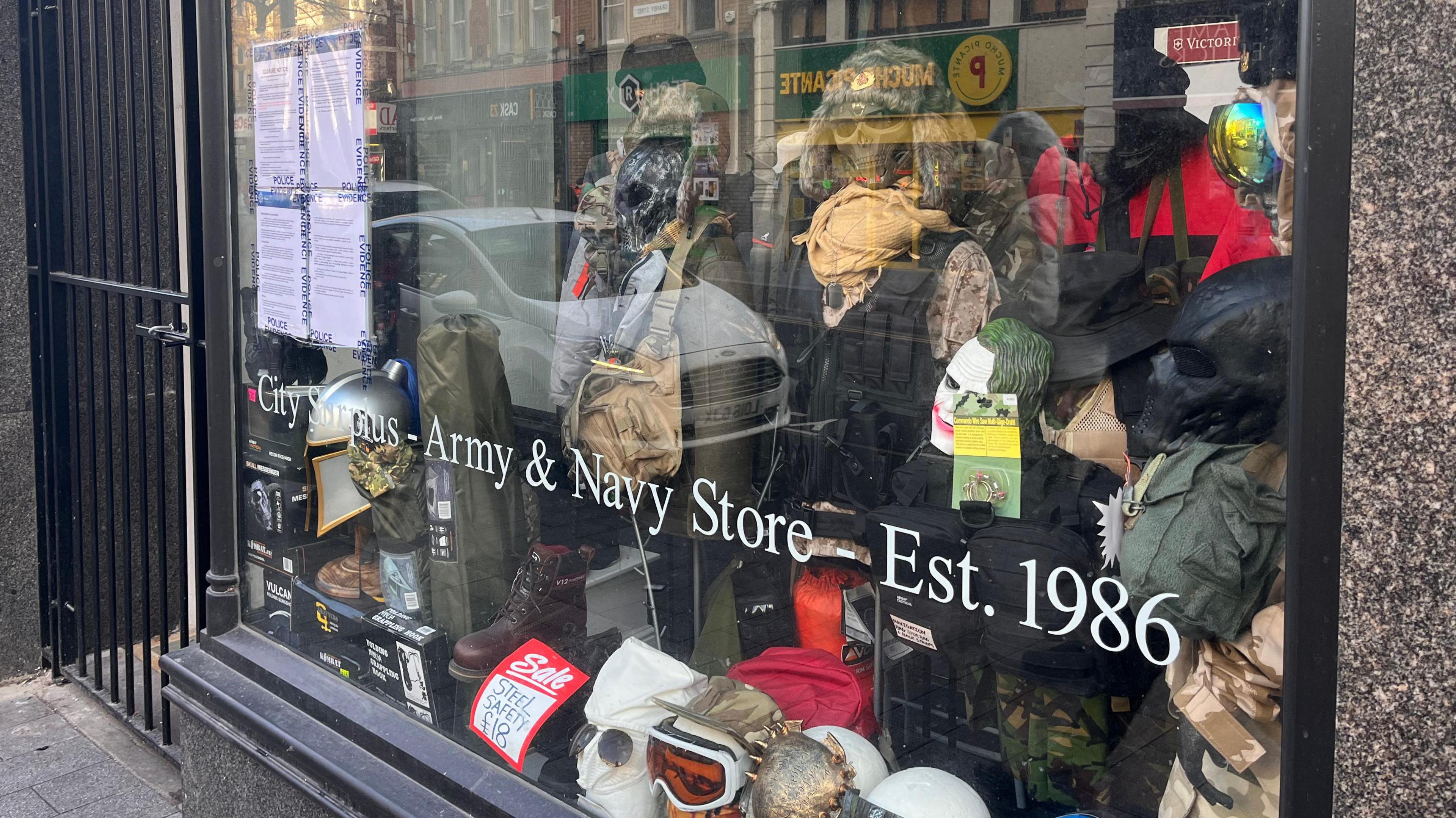 A shop window with four police noticed placed in it.  In the shop are masks and military headwear