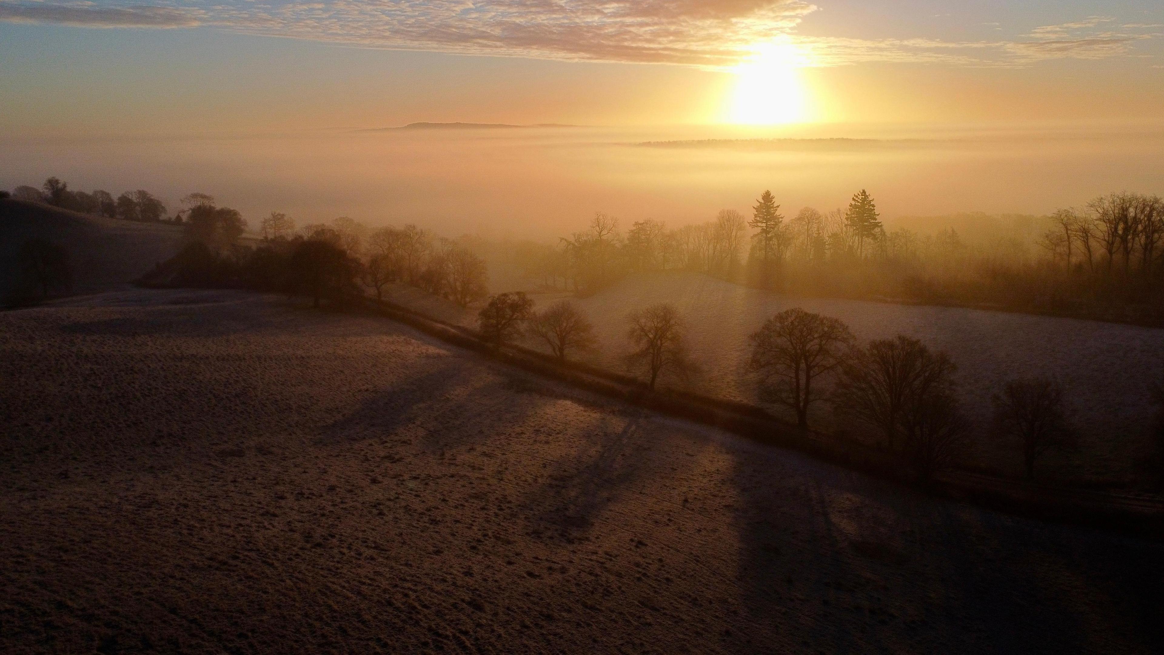 An orange sunrise across countryside including frozen fields and trees