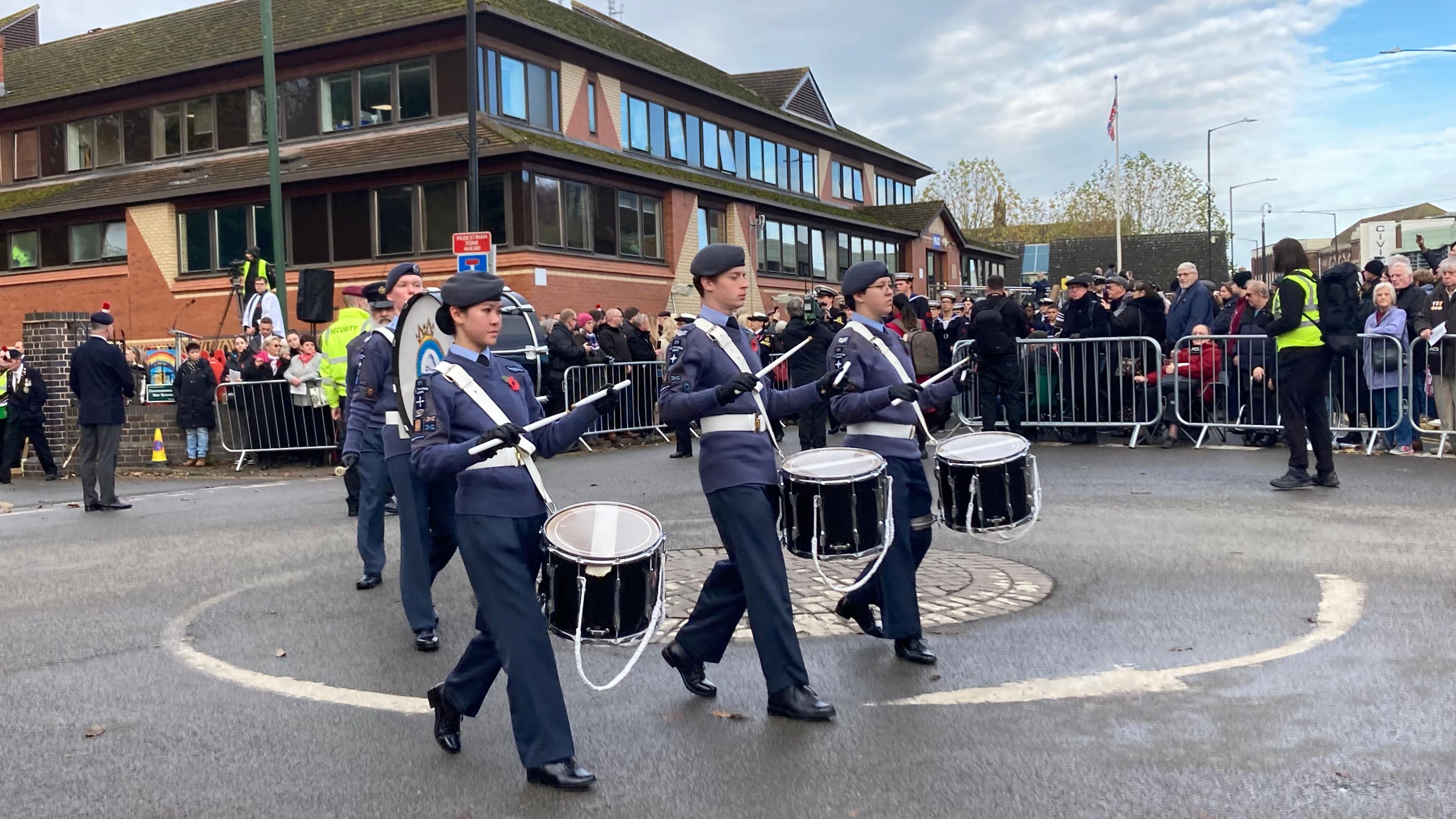 A parade featuring cadets playing drums marches through a town centre as part of Armistice Day celebrations.