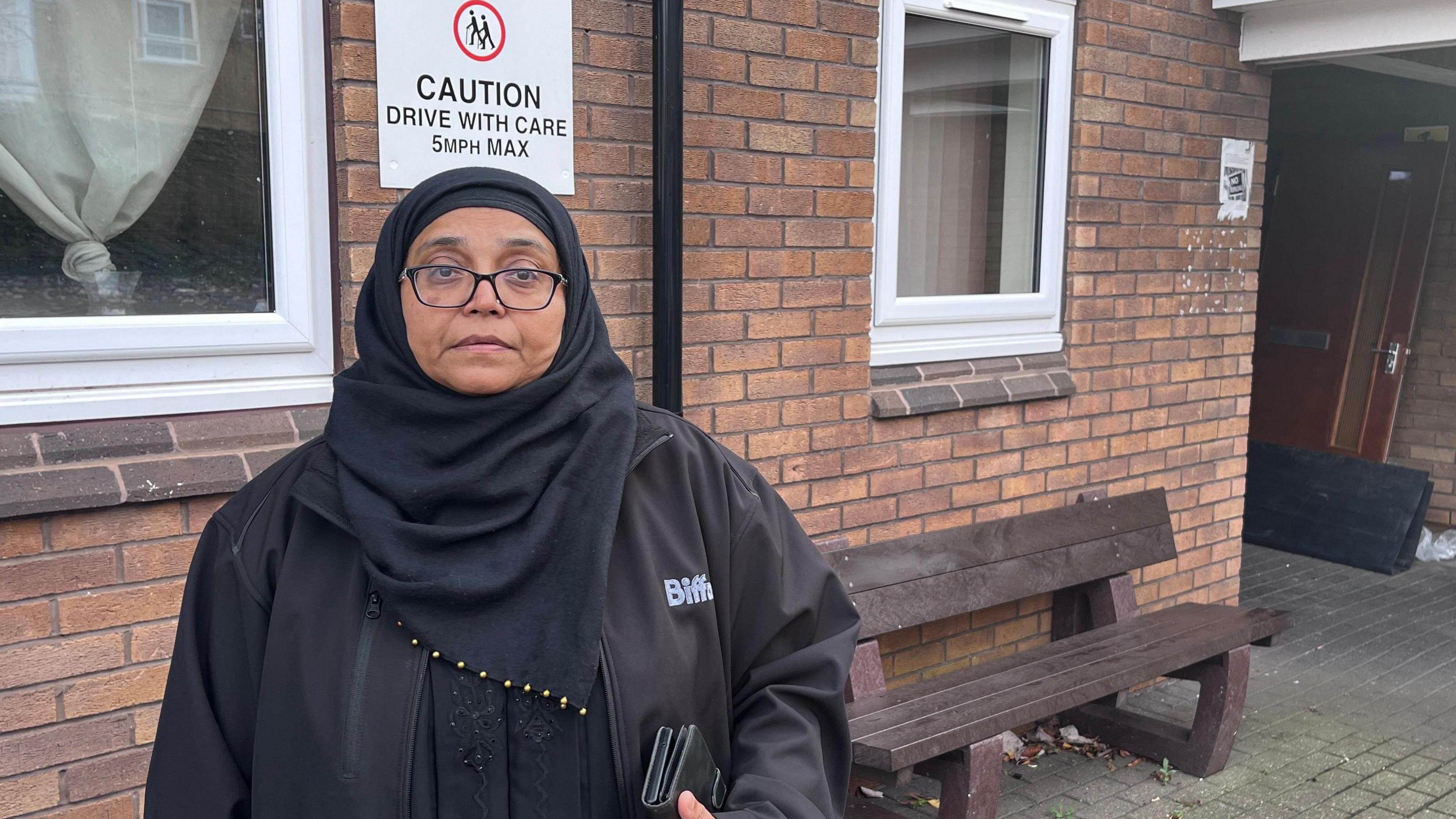 A woman in black wearing a black headscarf stood in front of the entrance to a block of flats