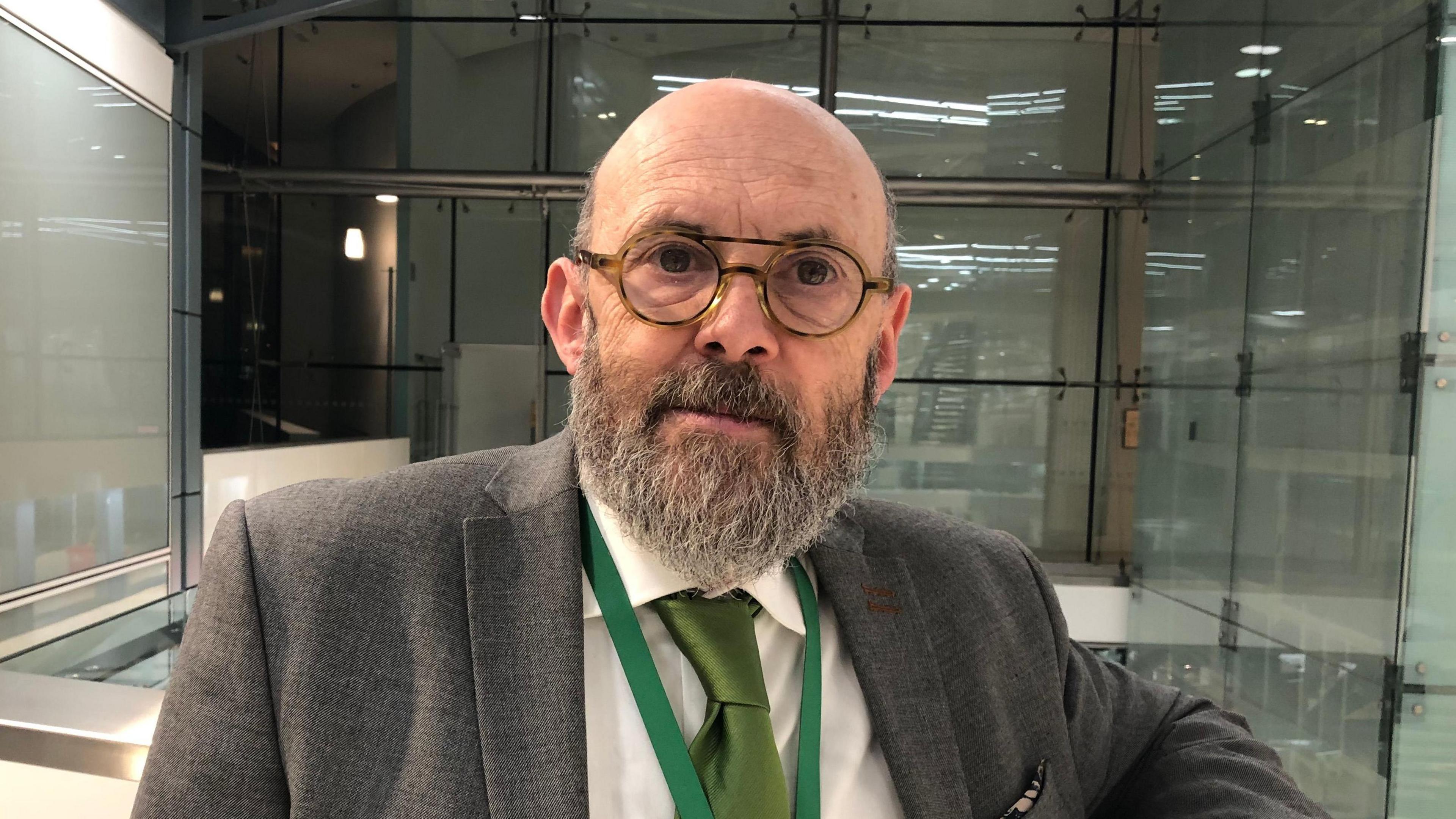 Andrew Stringer wearing glasses and a green tie in a glass building