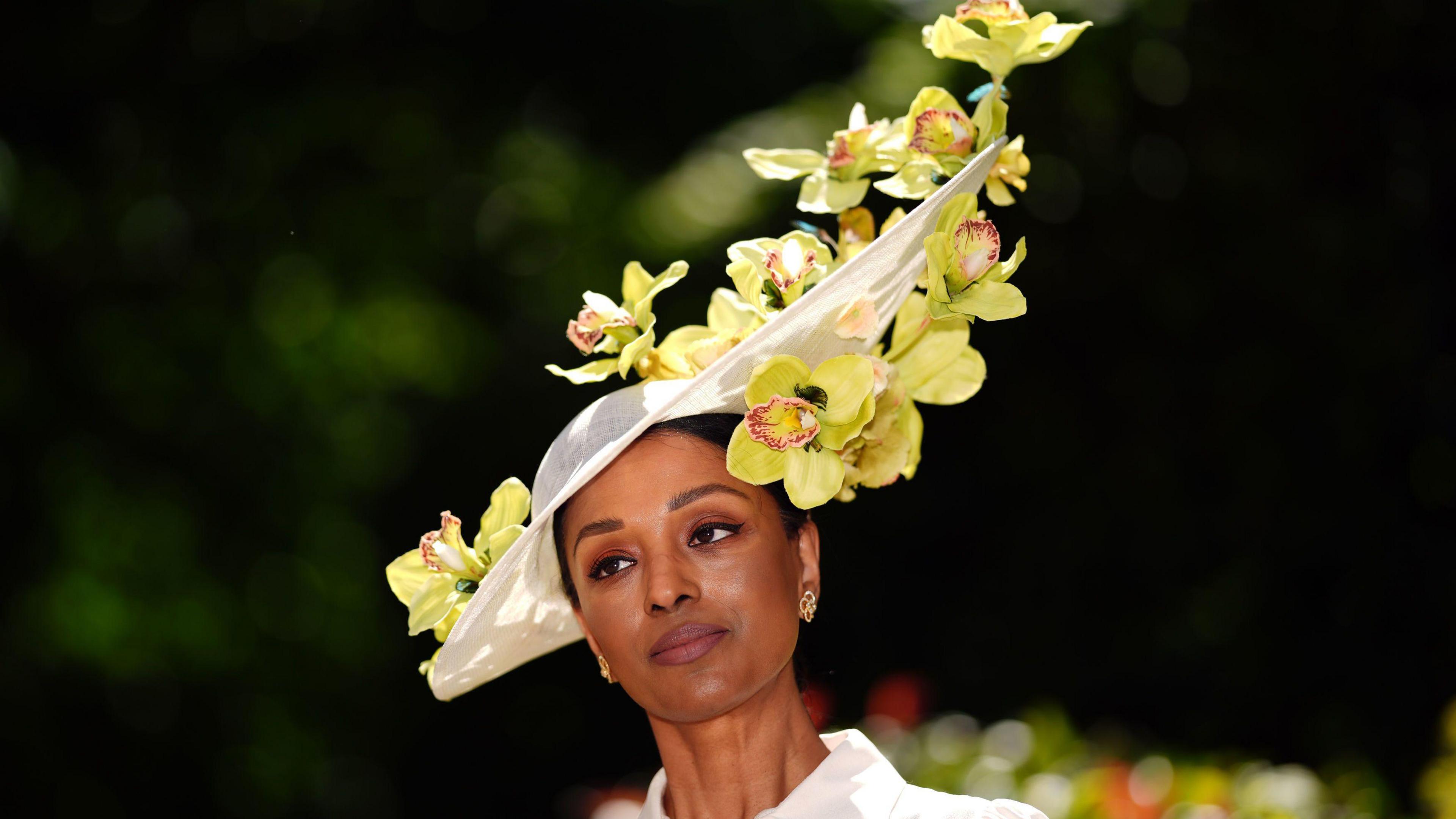 Woman poses for a photo wearing a white brimmed white headdress decorated with flowers