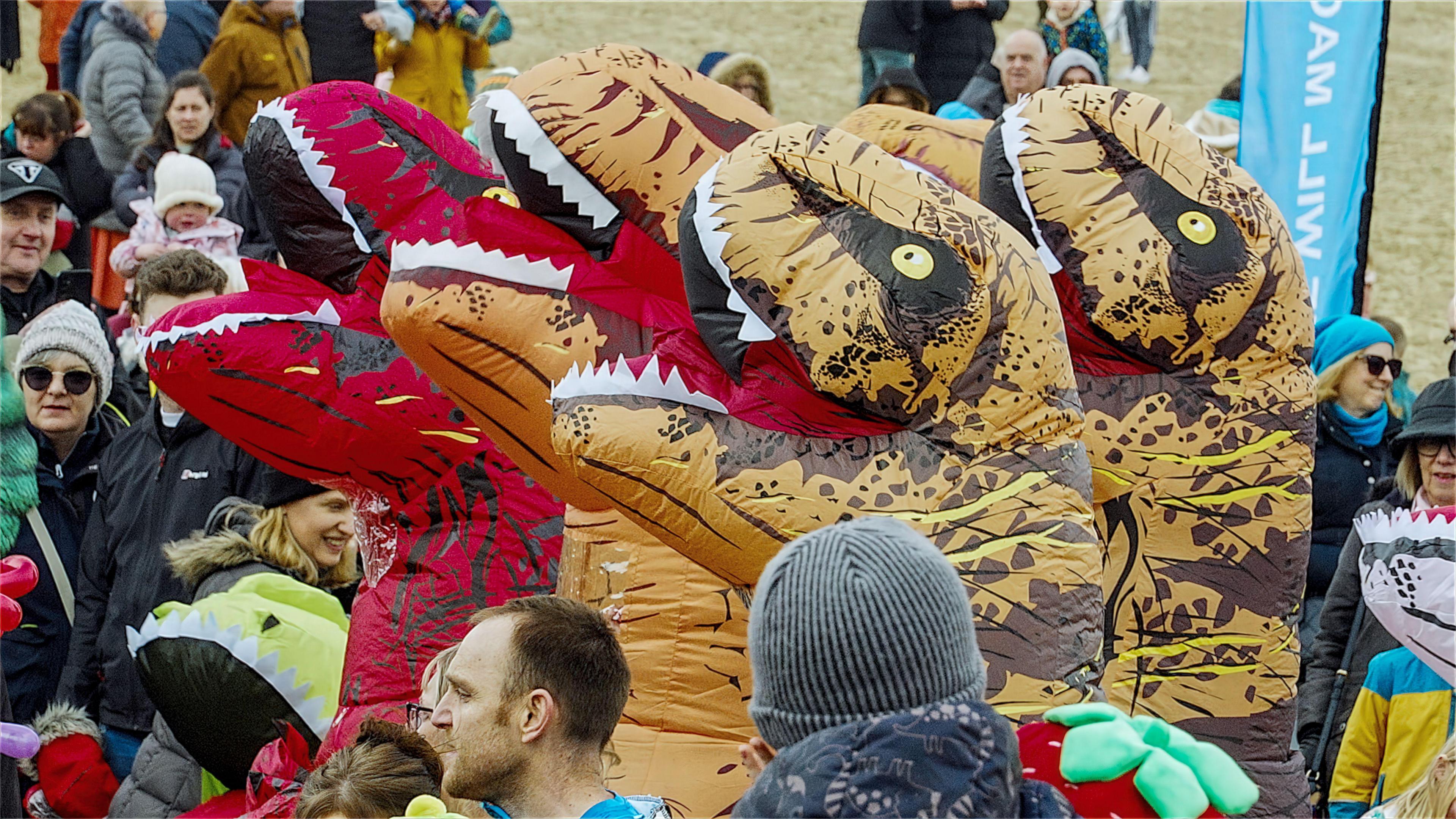 A crowd of people, with four people wearing tall dinosaur costumes towering over everyone else.