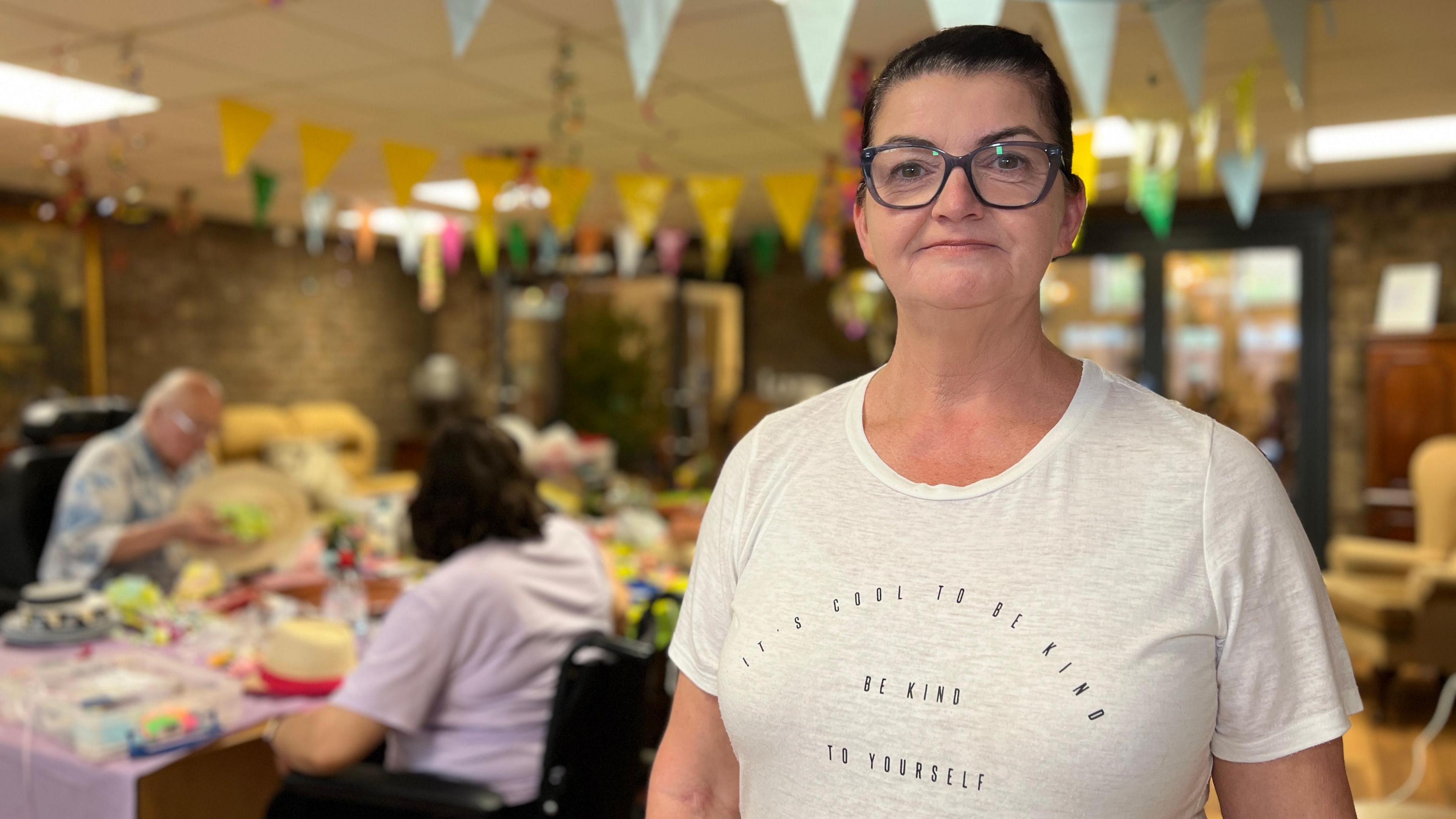 Aileen Landers looks at the camera as people work on the decorations behind her