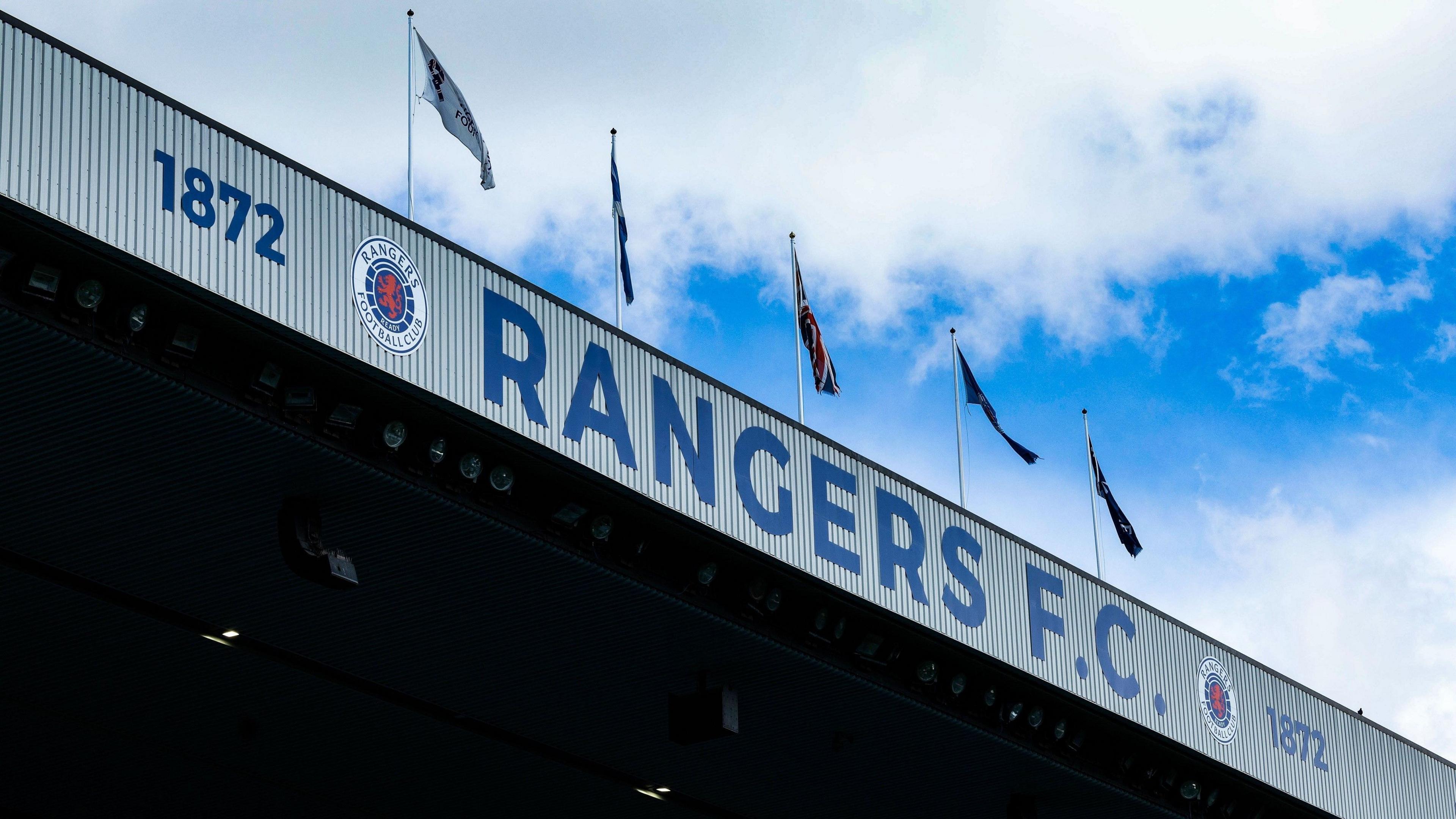 Rangers FC, the club logo and the year 1872 written on part of the Ibrox stadium. There are flags flying above the sign