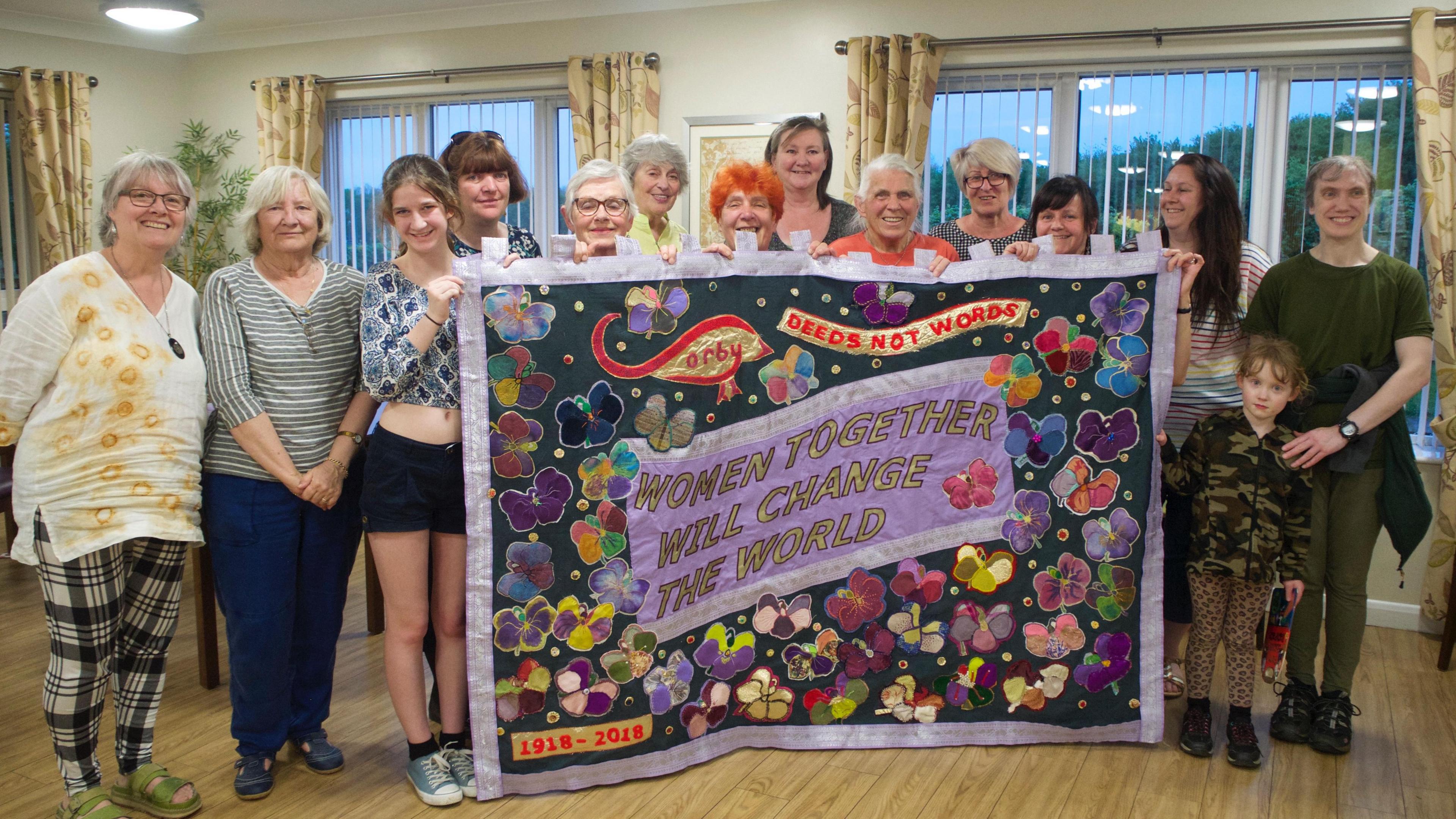 A group of women hold a brightly decorated banner