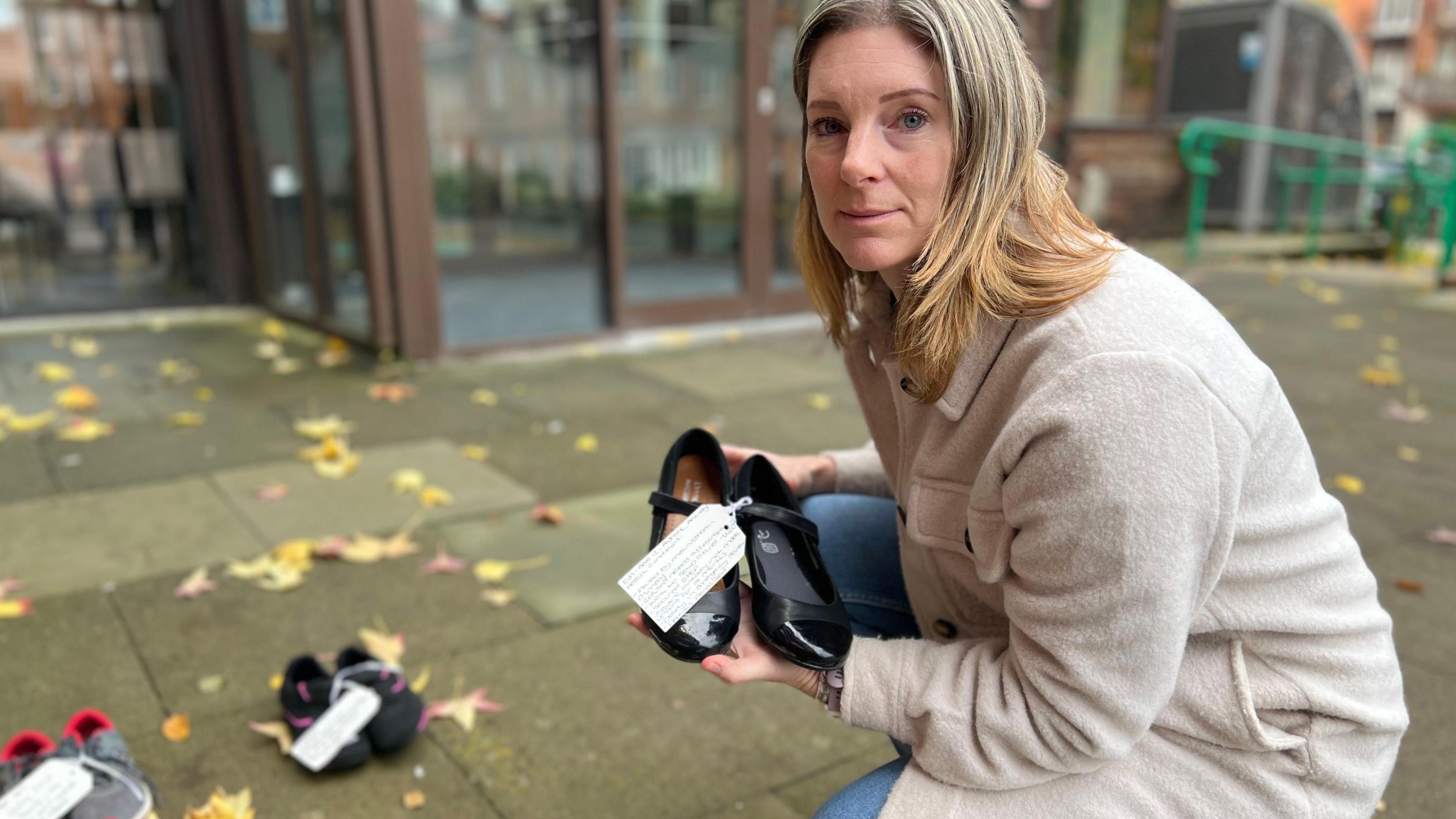 Marie Llewellyn crouching down placing a pair of black shoes, with a label