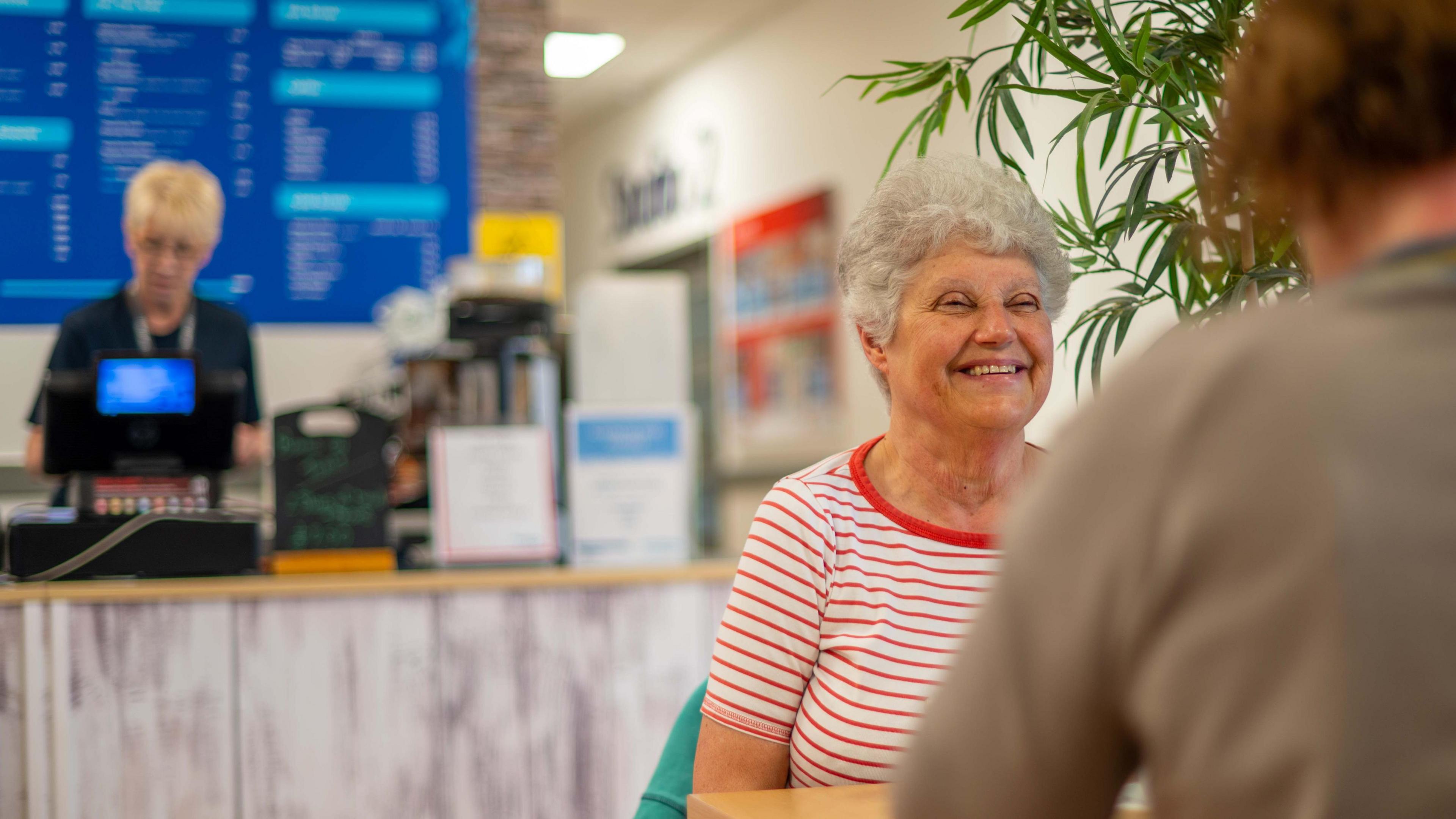 Picture of two women sitting having coffee at the Horizon cafe, in the background a lady behind the till.