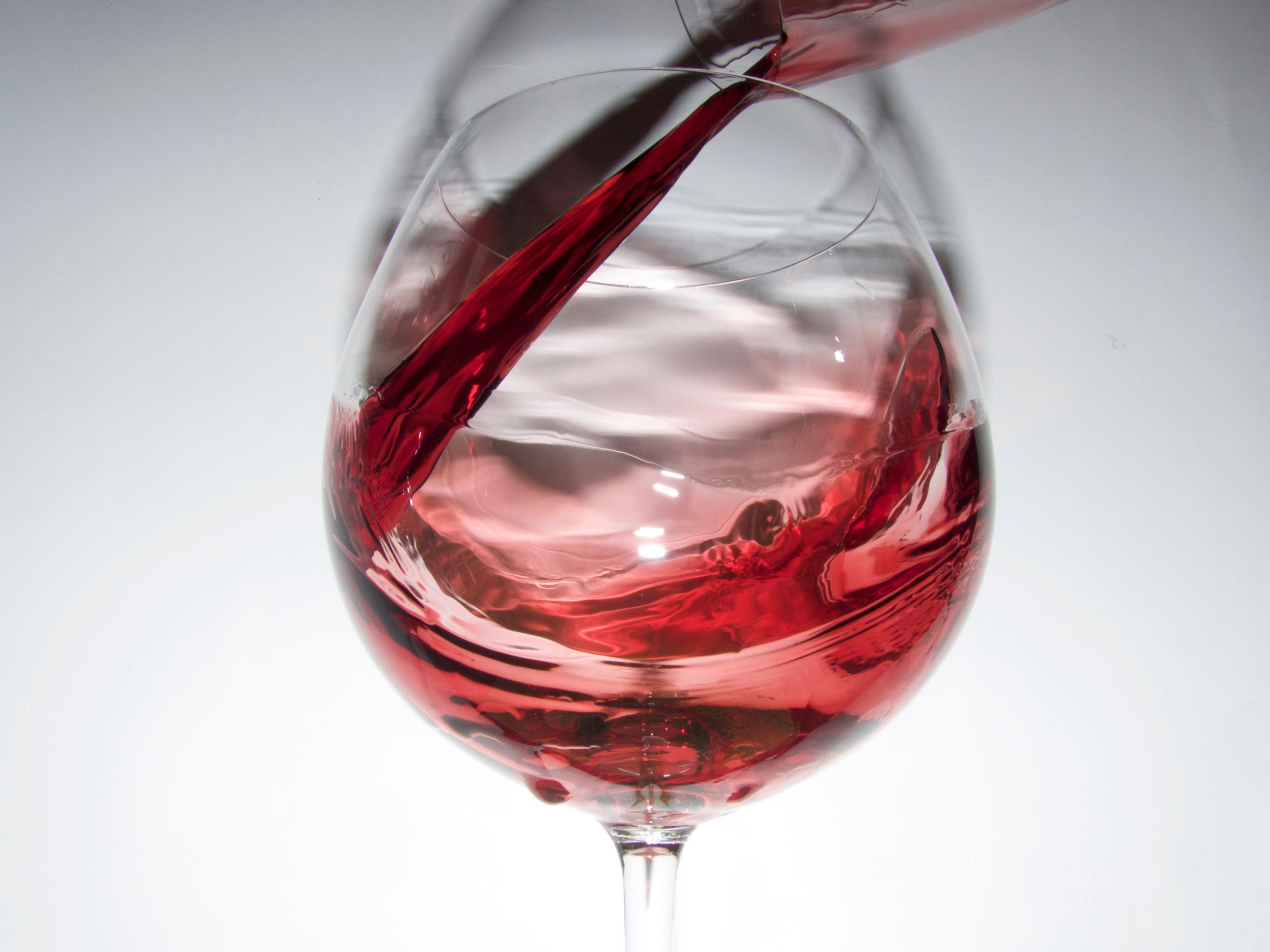 Red wine swirls in a wine glass. The background is white.