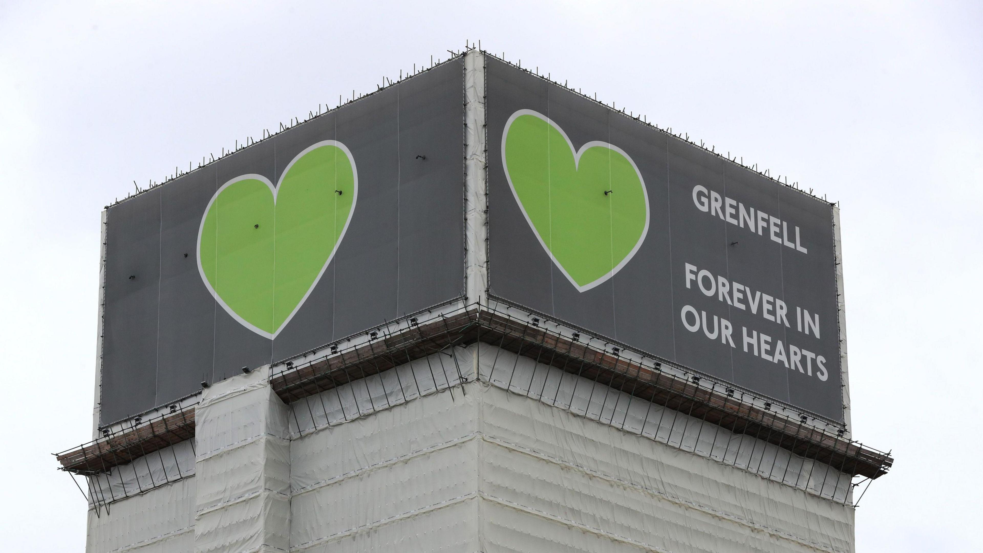 File photo from 2021 showing a covered Grenfell Tower with grey billboards  at the top featuring green hearts and the message 'Grenfell - forever in our hearts'