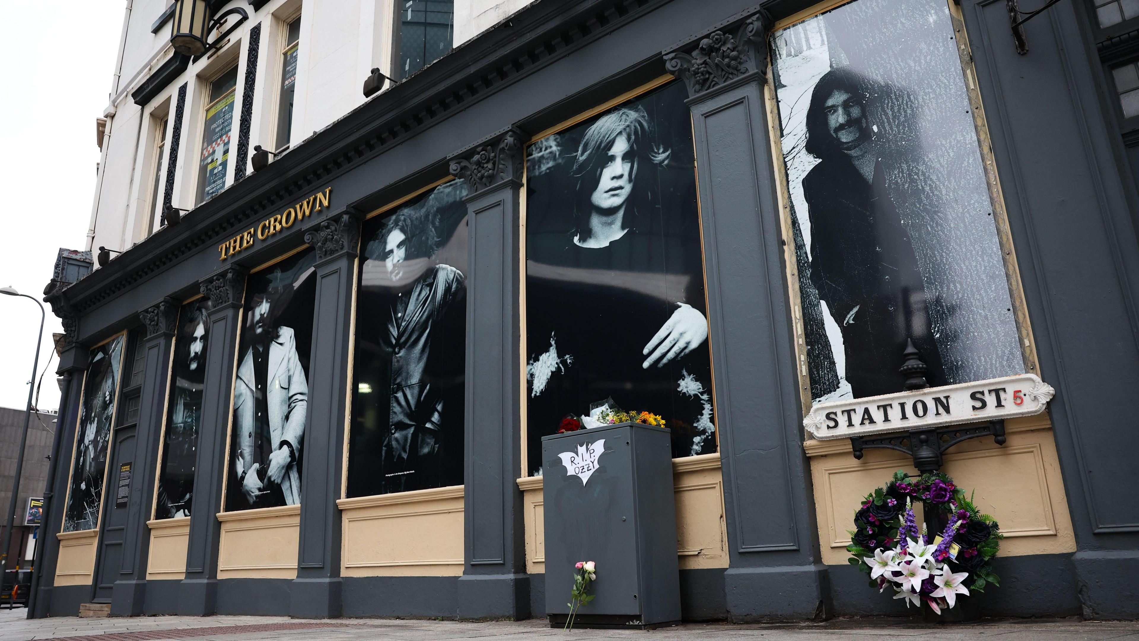 Black and white images of four young men adorn the outside of a pub. All of them have long hair, three have big moustaches.
