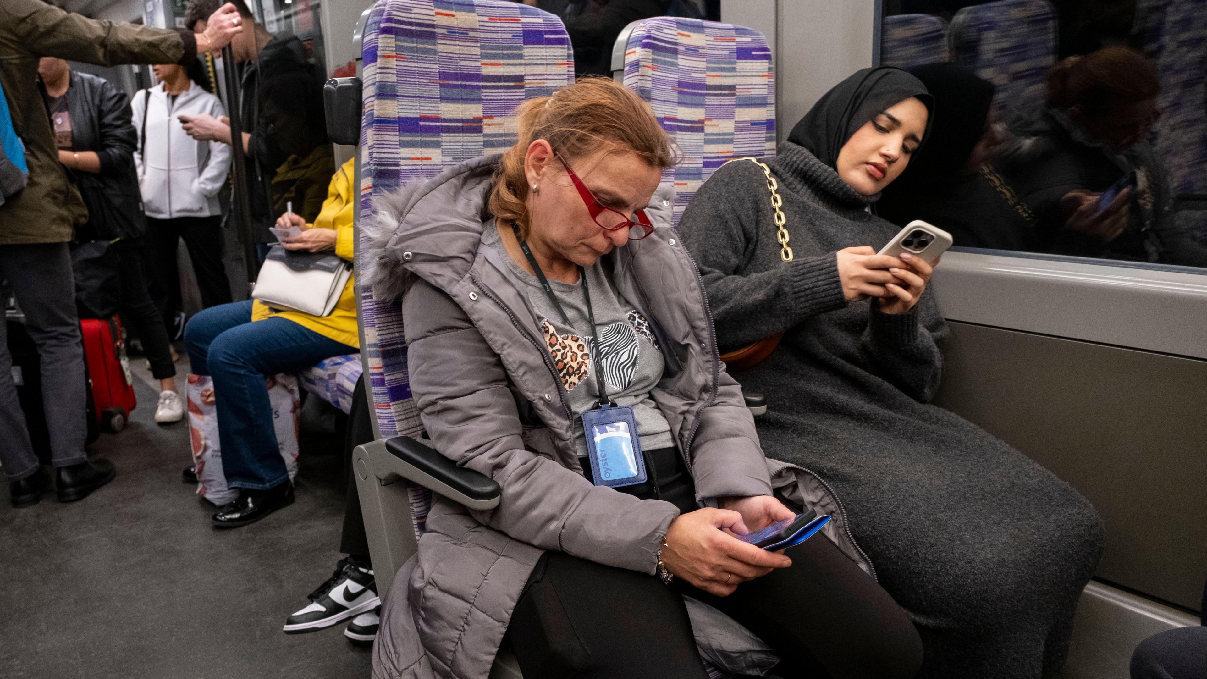 Two women on Elizabeth line using phones