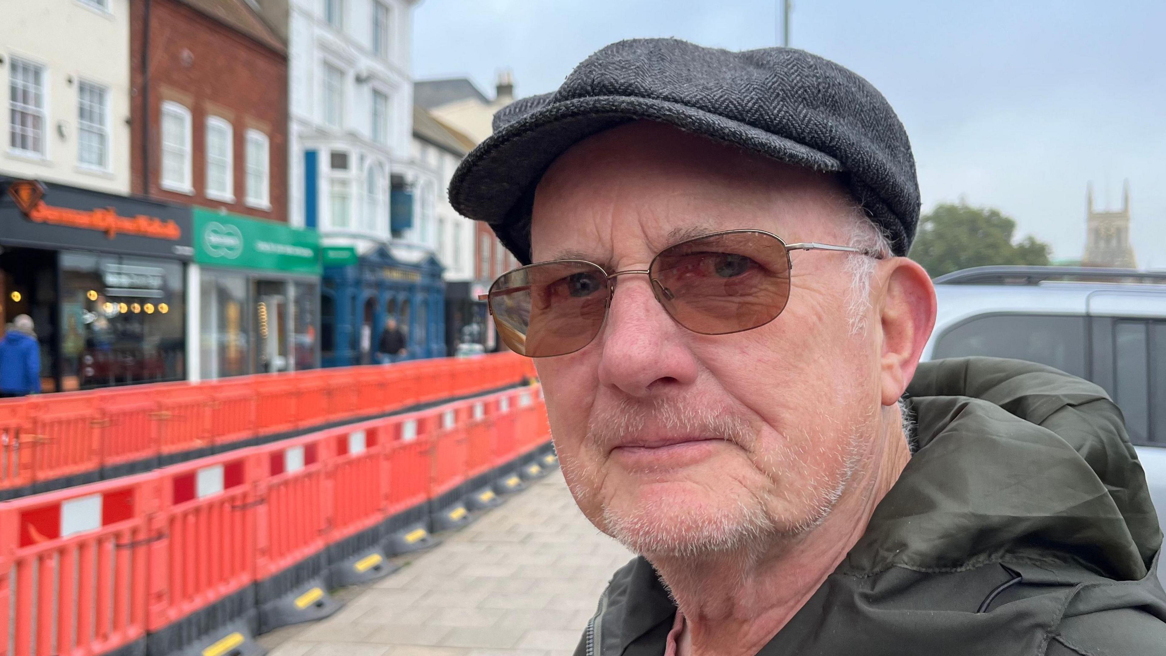 Stephen Lucas in Great Yarmouth town centre. He is wearing sunglasses, a grey flat cap and green anorak.