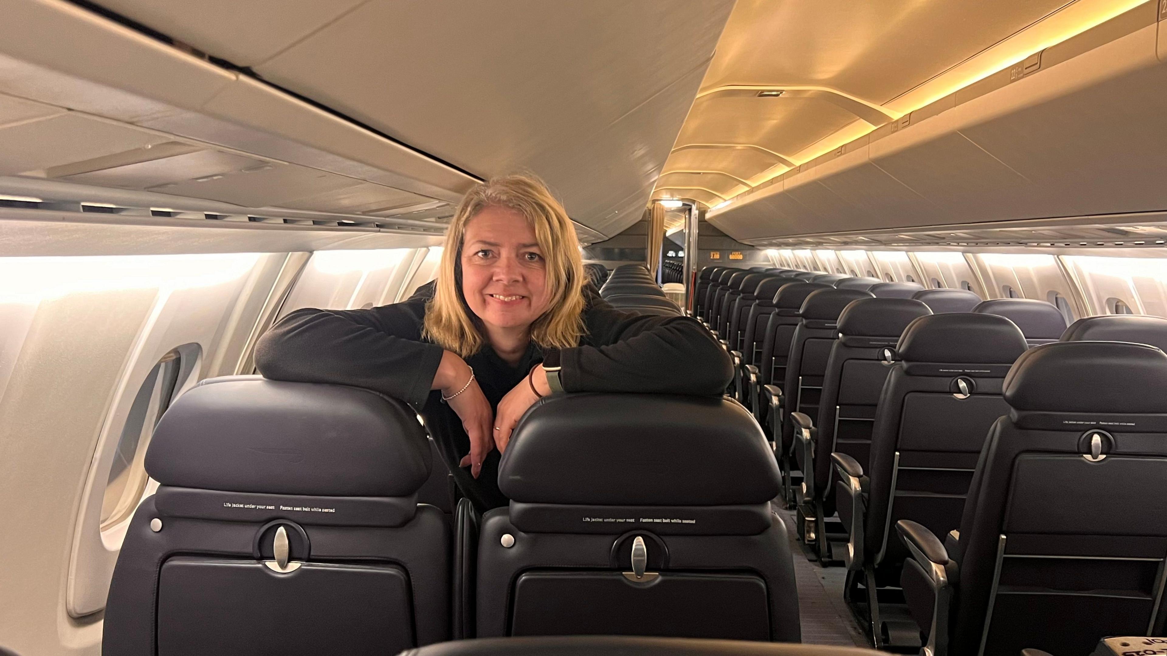 Carolynne Hutchins leaning on one of the dark-coloured leather seats inside the aircraft. She is smiling and looking towards the camera.