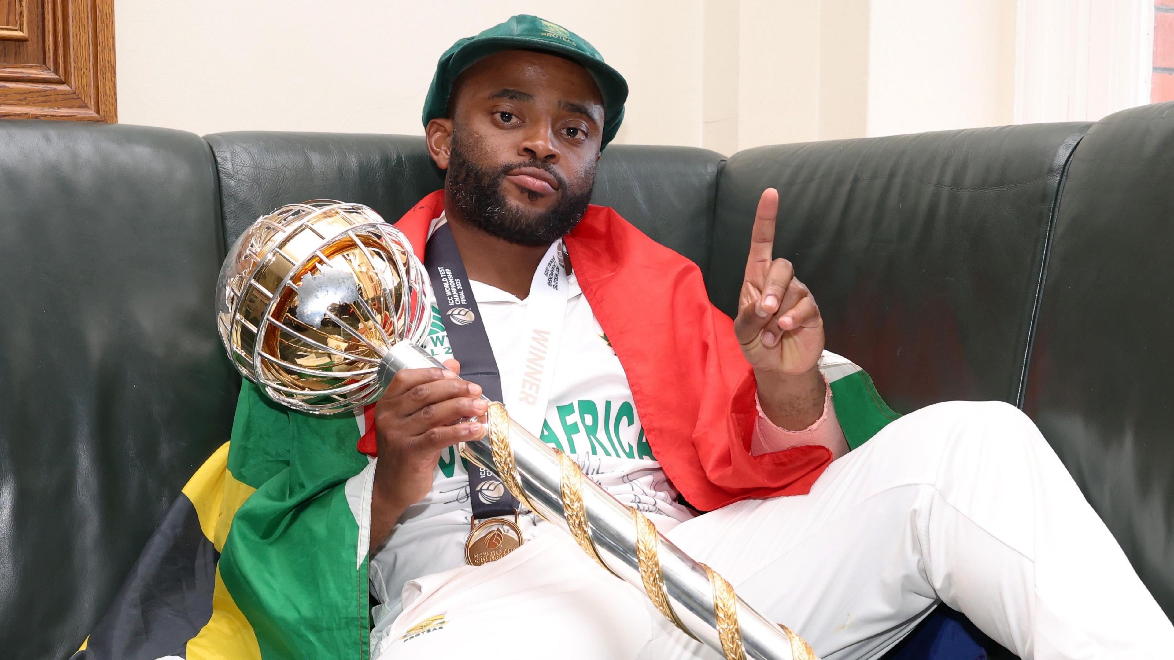 South Africa captain Temba Bavuma, draped in a flag, holds up one finger as he celebrates winning the World Test Championship final