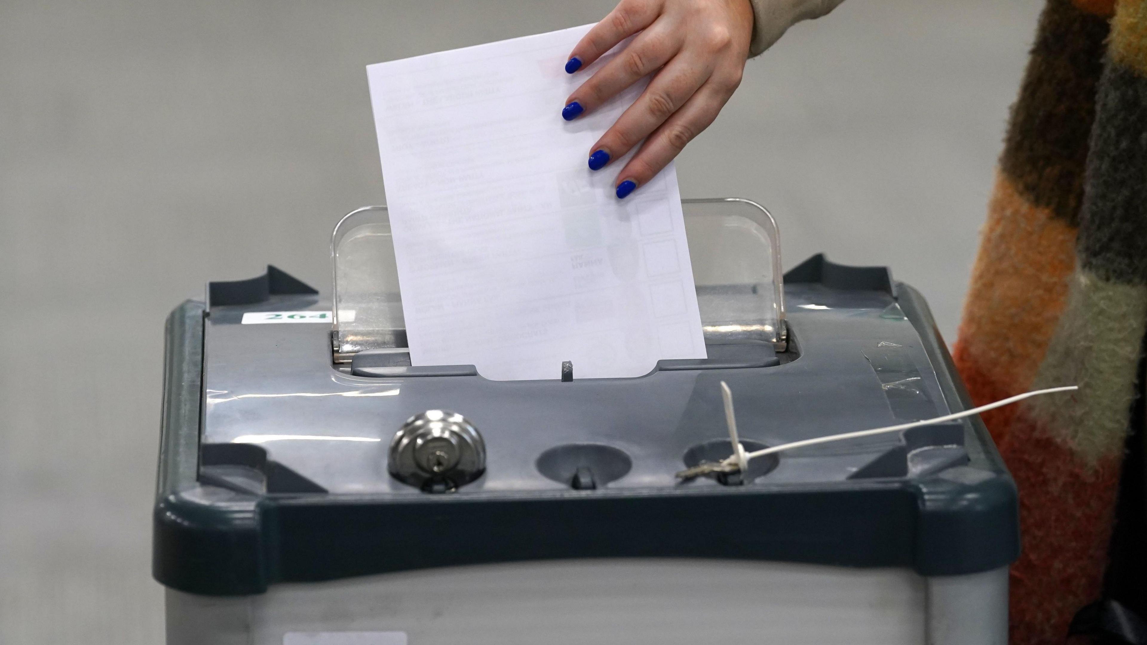 A woman places a white ballot paper into a vote box